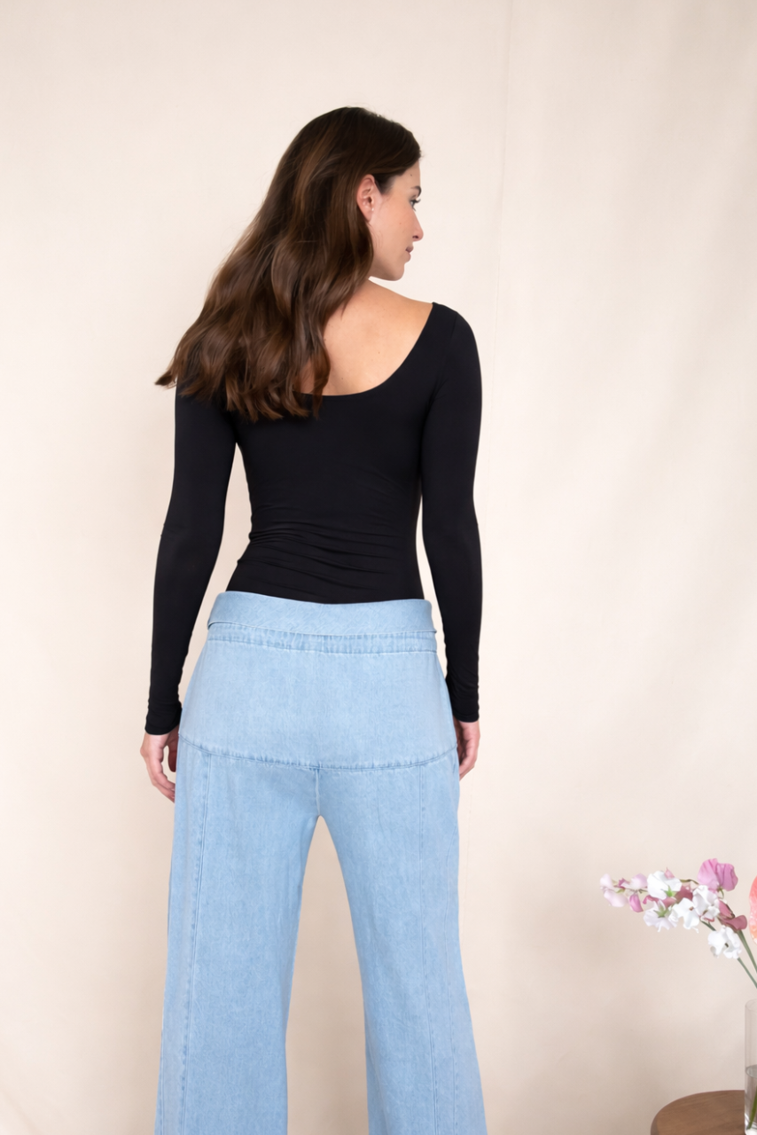 Woman wearing a black bodysuit and light blue jeans against a beige background