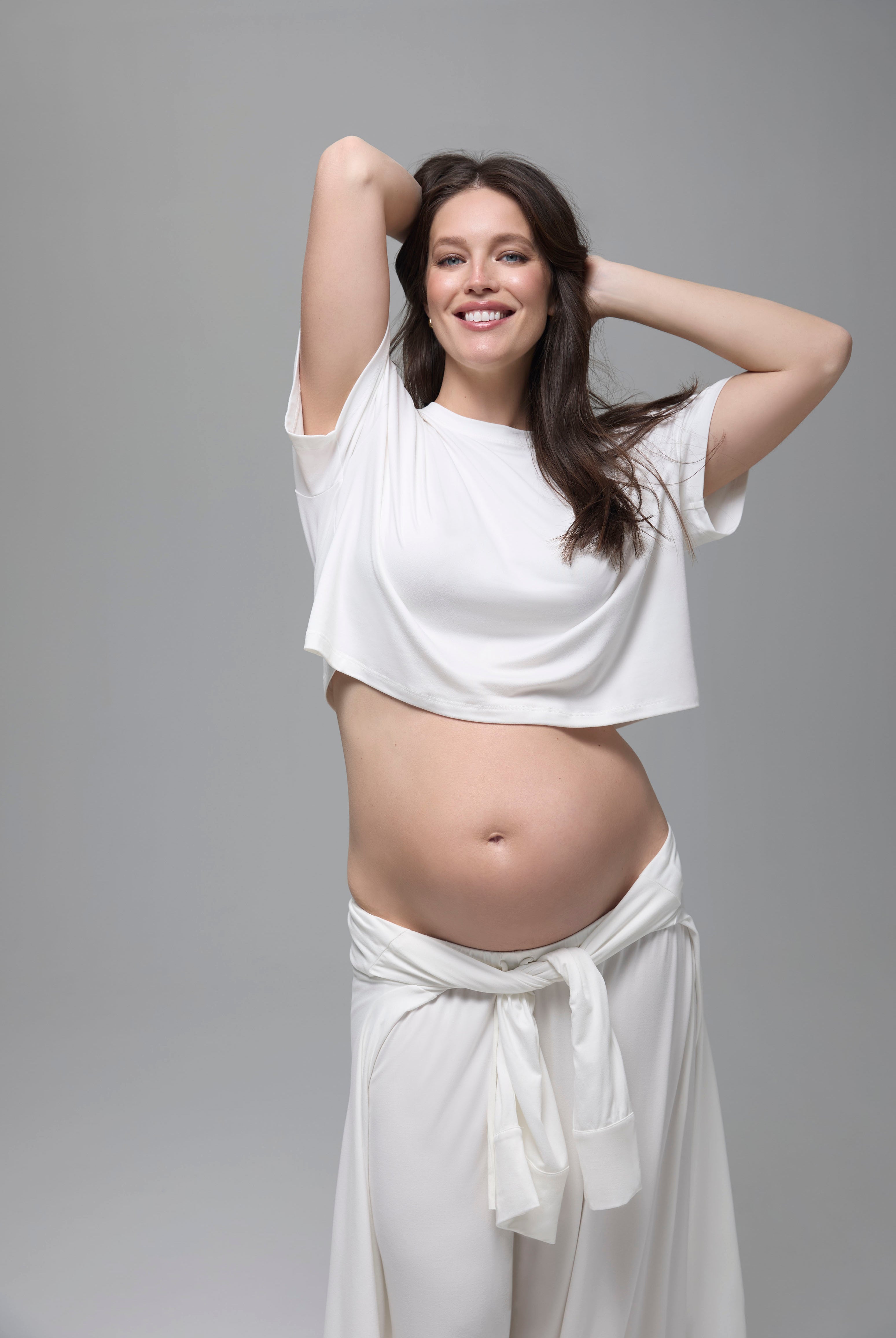 Pregnant woman wearing a white outfit against a gray background
