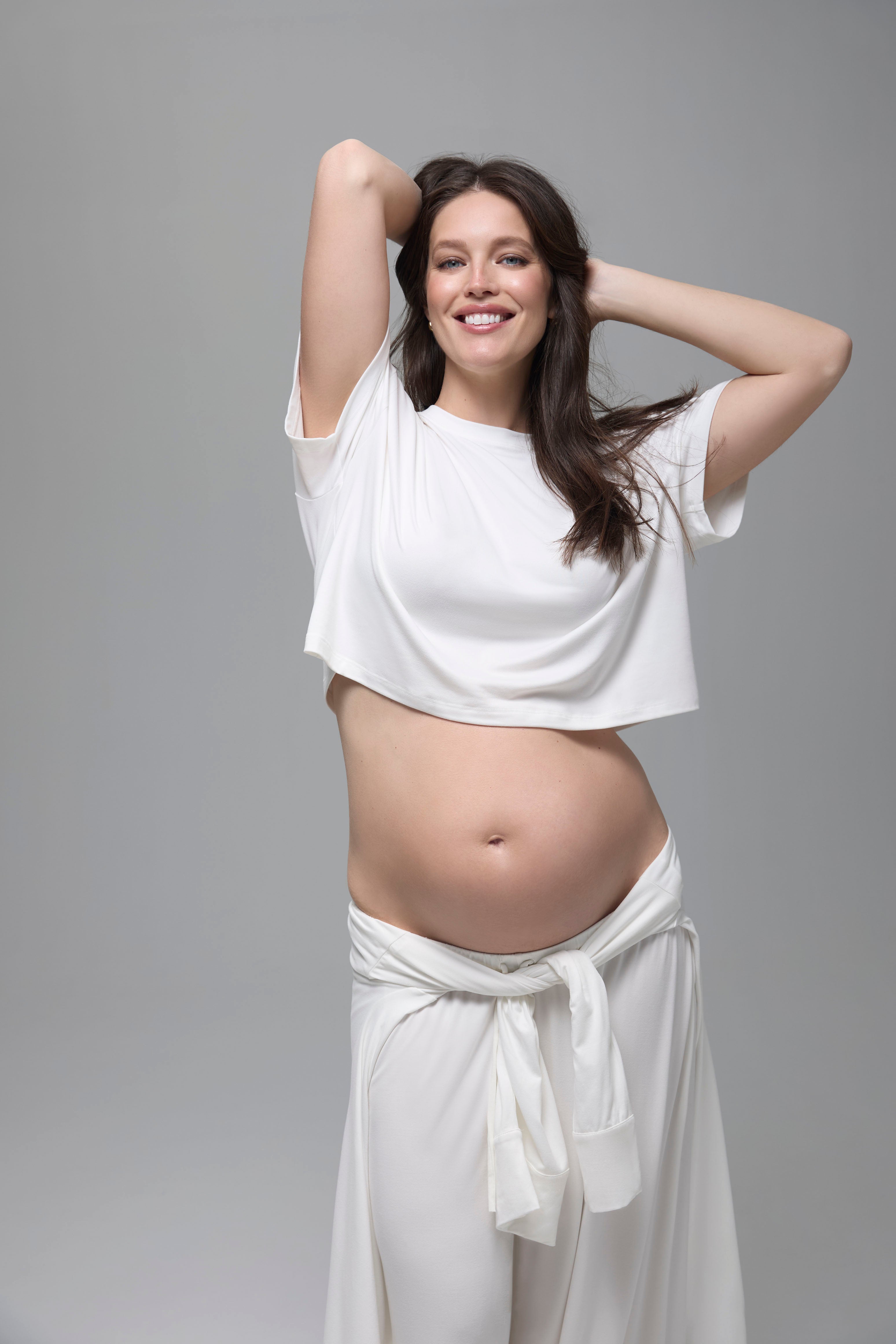 Pregnant woman wearing a white outfit against a gray background