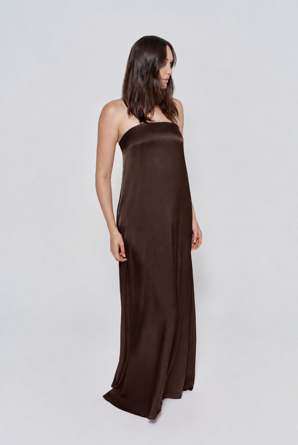 Pregnant woman wearing a Bumpsuit brushed satin gown in a chocolate color against a white background