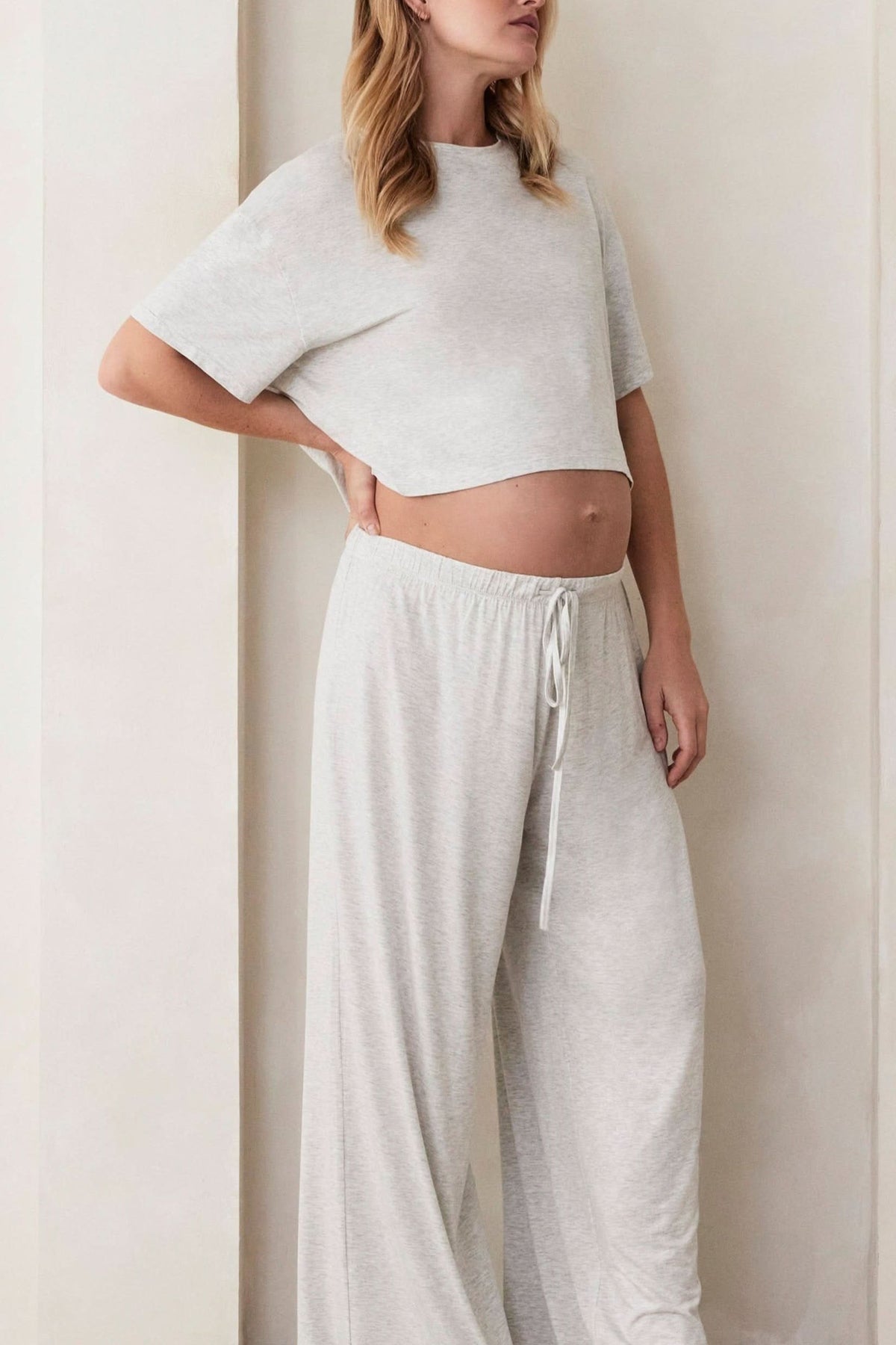 Three-quarter view of The Cotton Cloud Crop Tee in heather grey, showing its cropped relaxed fit and short sleeves on a model indoors