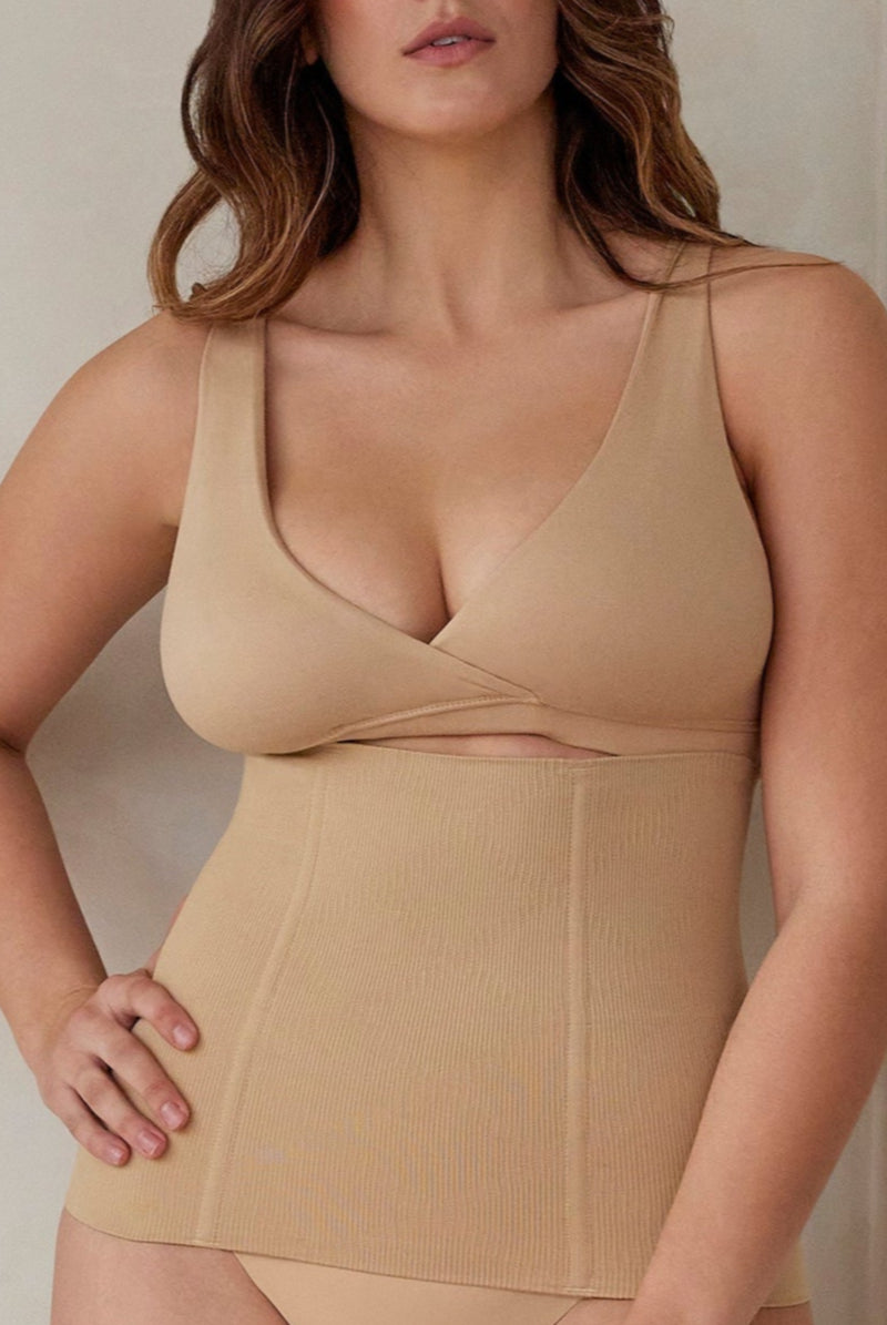 Woman wearing a beige shapewear garment against a neutral background