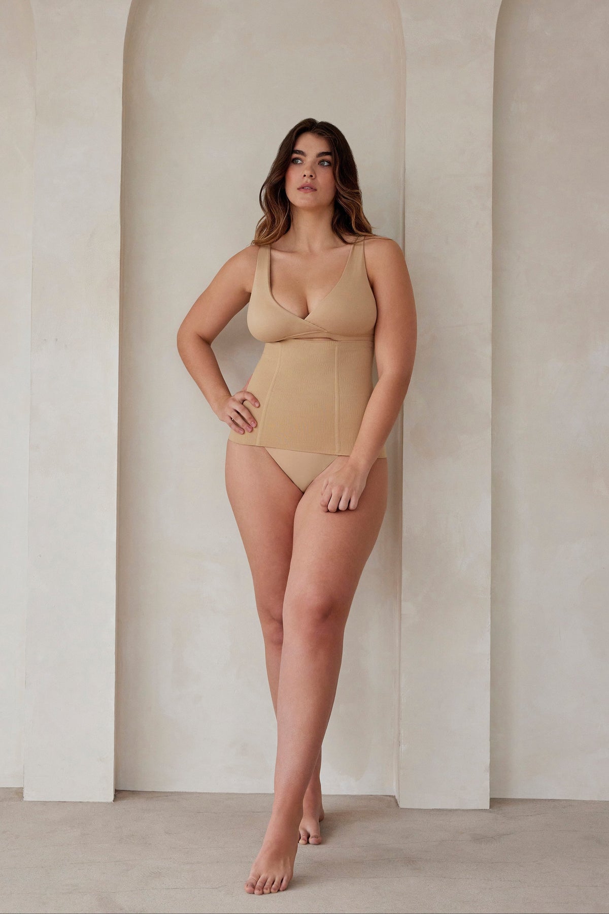 A woman wearing a beige reversible comfy bra and support waist trainer by Bumpsuit