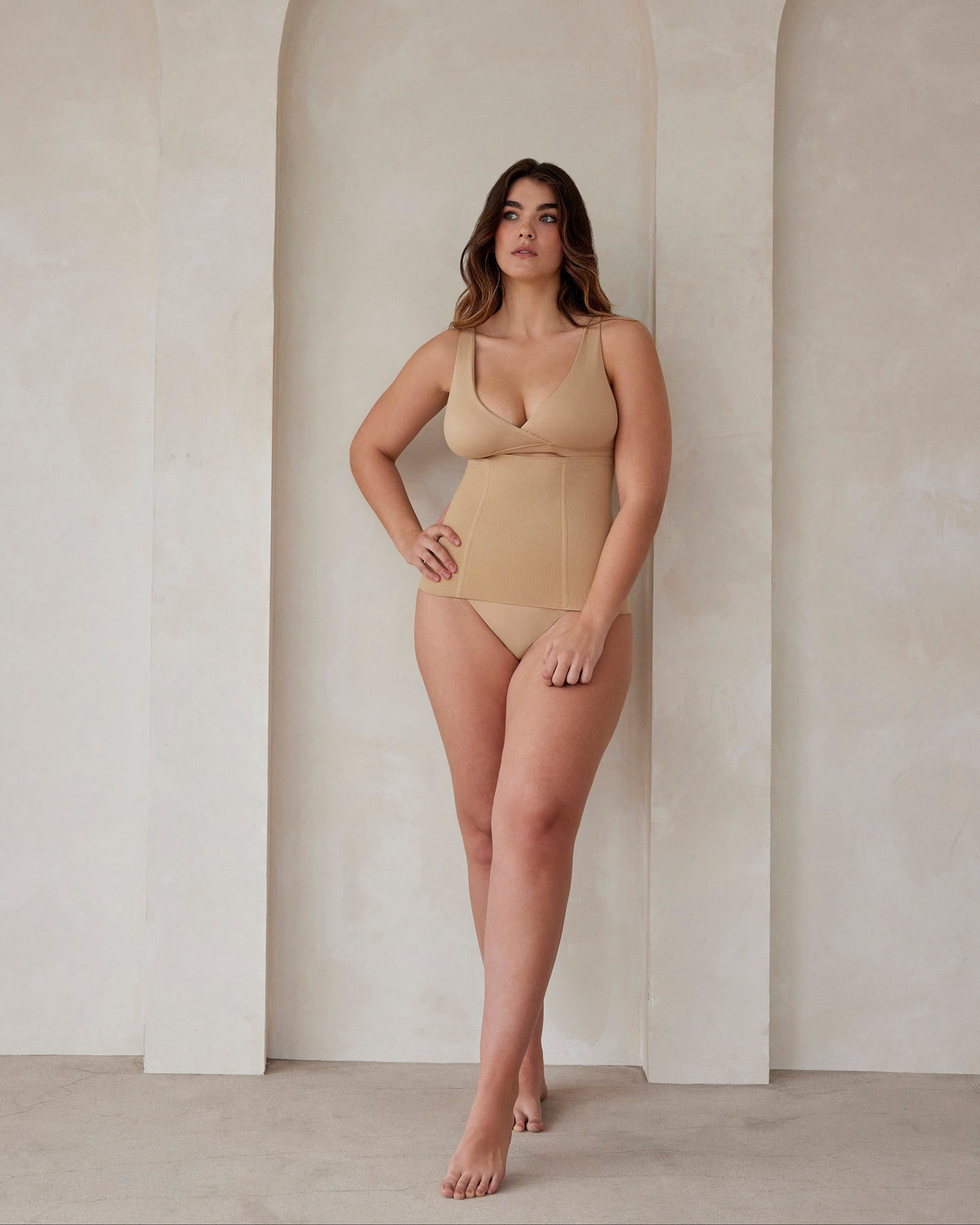 A woman wearing a beige reversible comfy bra and support waist trainer by Bumpsuit