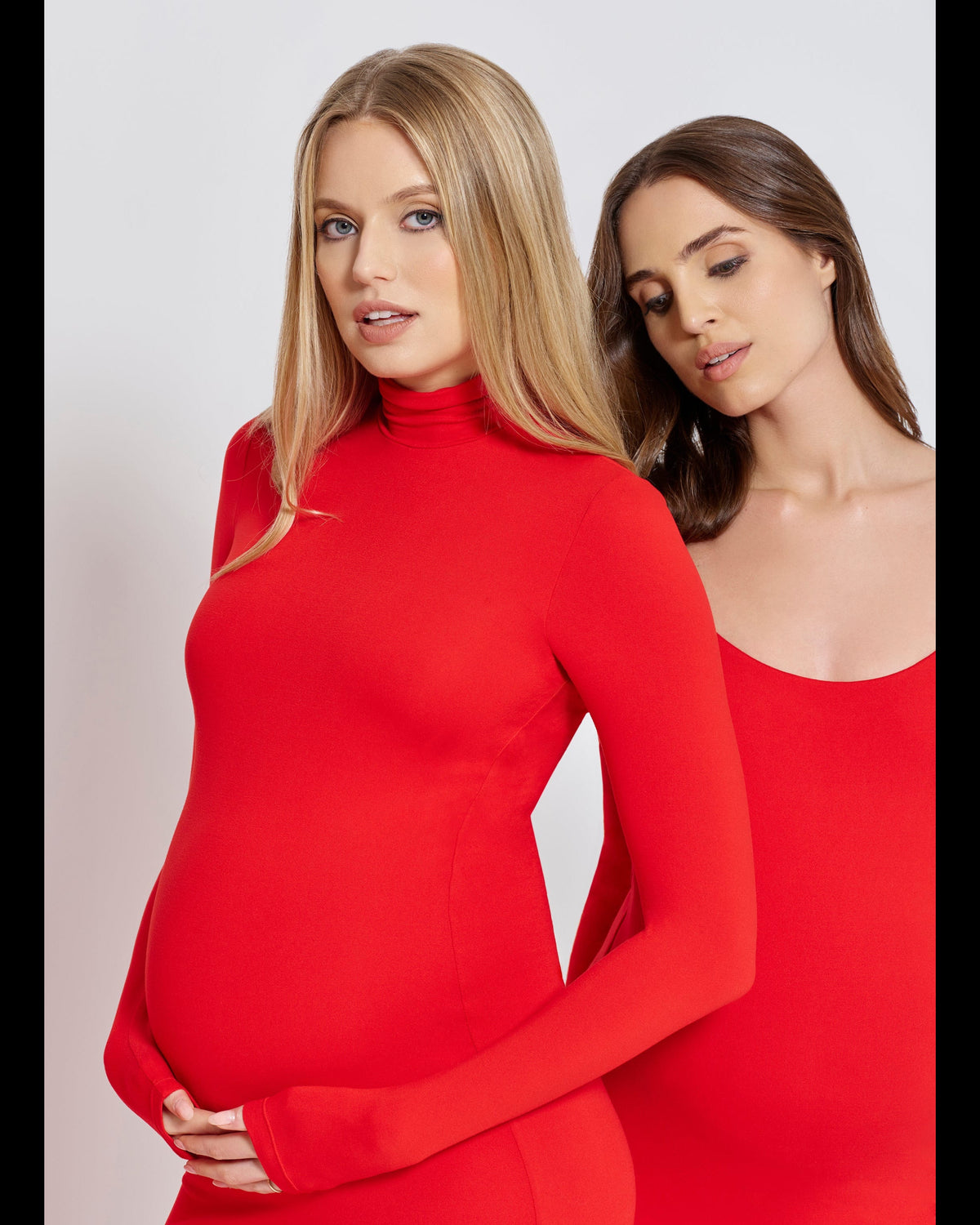 Two pregnant women wearing red dresses against a white background