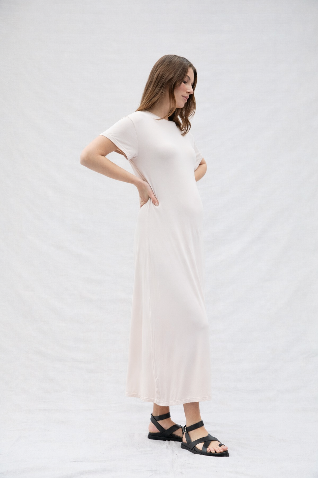 Pregnant woman wearing a oat coloured dress on a plain background