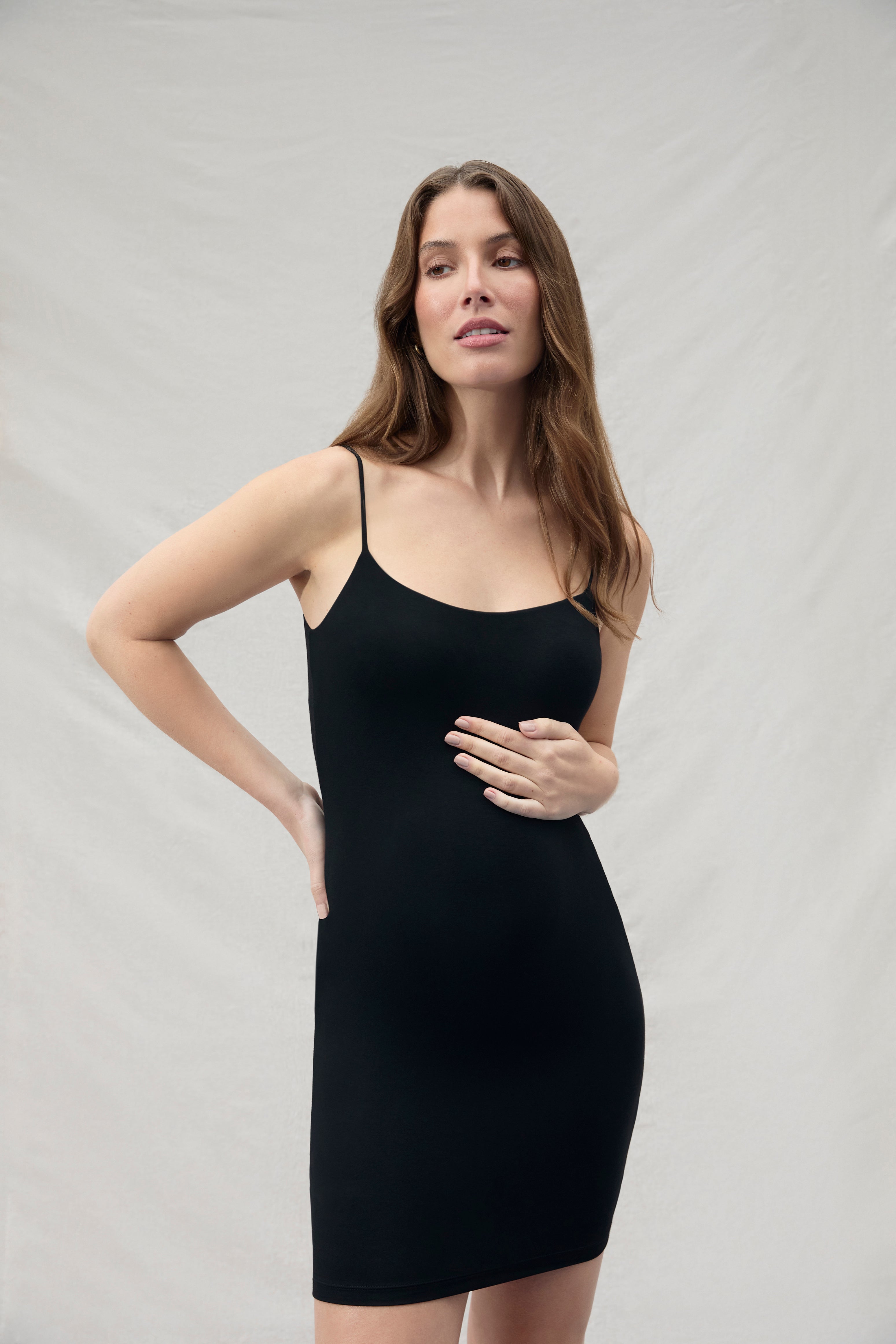 Woman wearing a mini black slip dress against a plain background