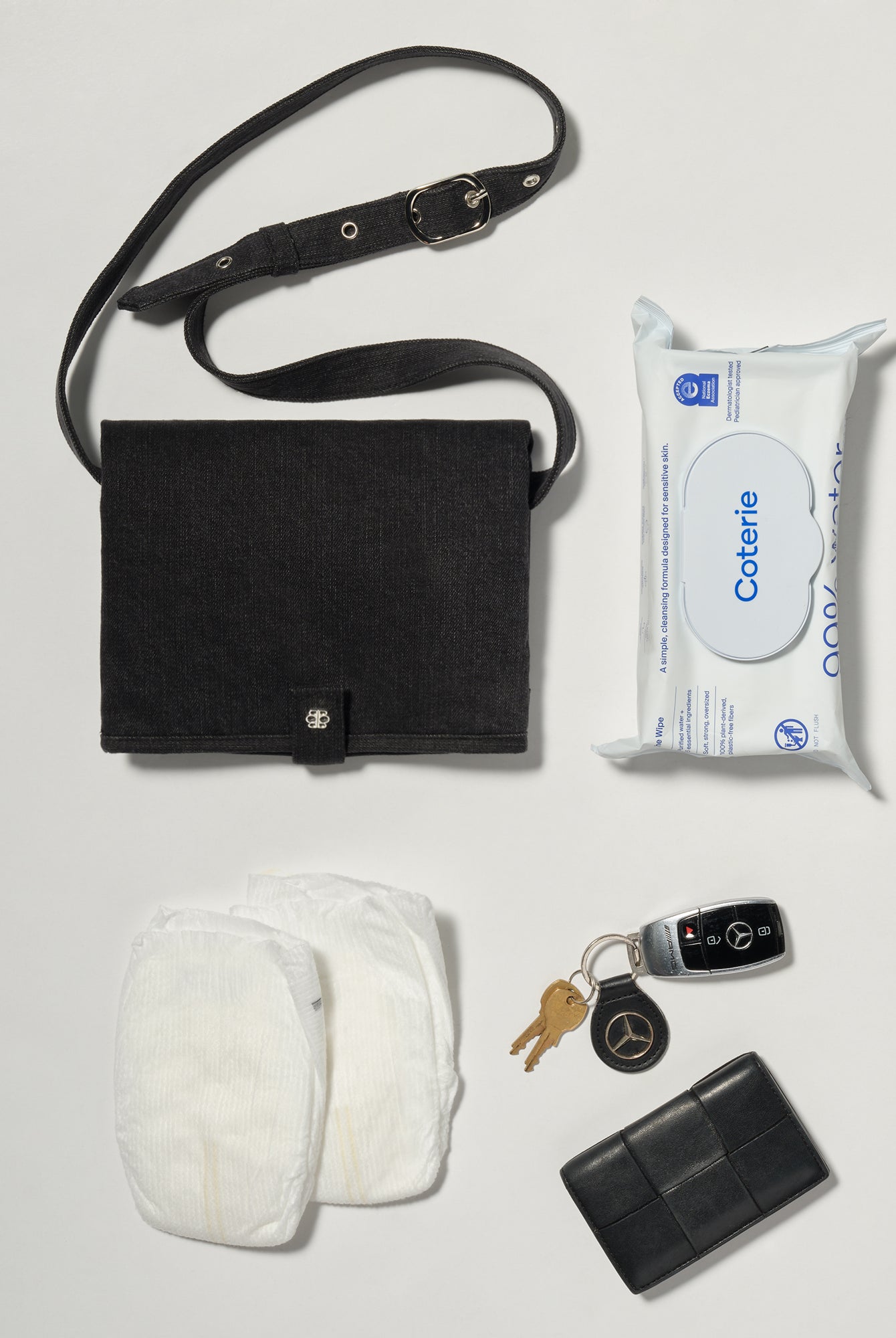 A black denim roll up diaper change mat bag by Spell and Bumpsuit,, shown on a light gray background with wipes and diapers keys and wallet