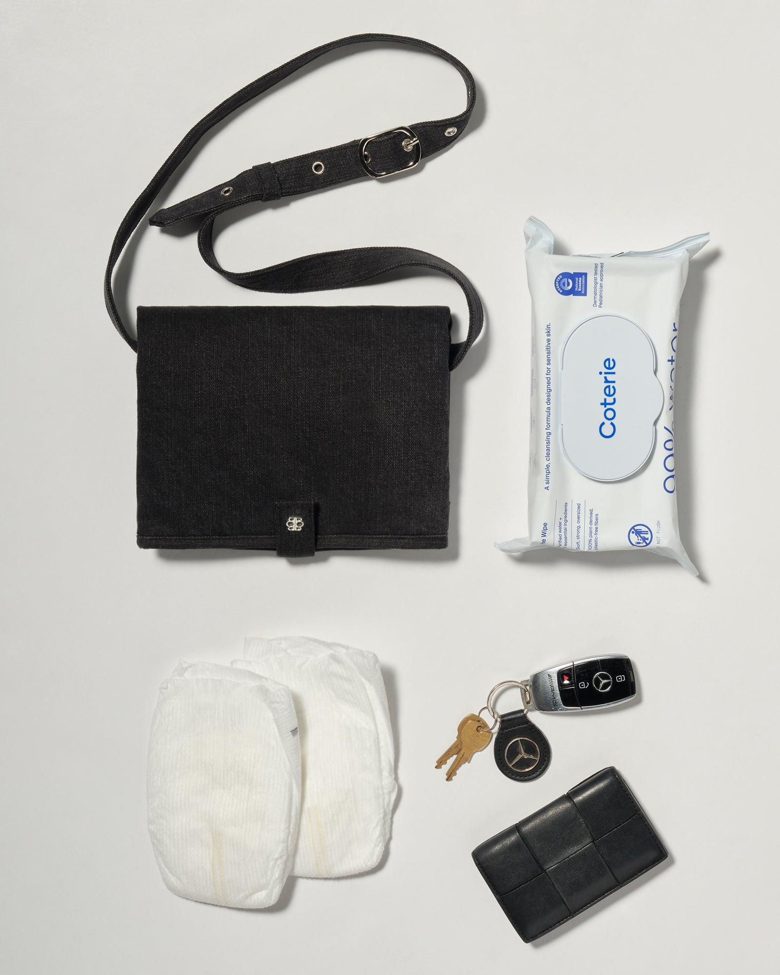 A black denim roll up diaper change mat bag by Spell and Bumpsuit,, shown on a light gray background with wipes and diapers keys and wallet