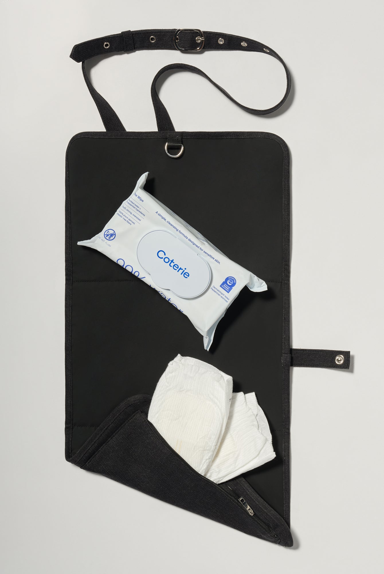 A black fabric diaper bag or organizer pouch with a top strap, shown on a light gray background. The pouch has a front pocket holding a package of baby wipes and a white diaper hanging below.