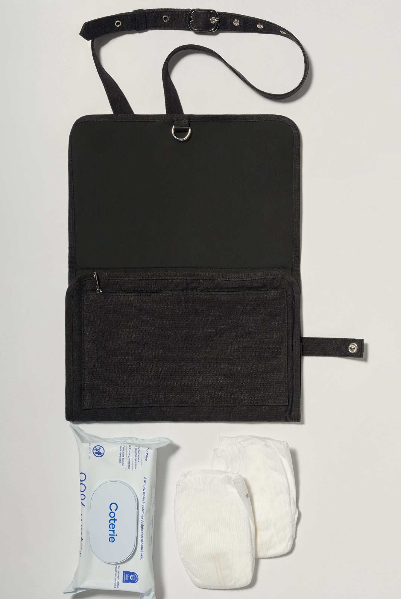 A black denim roll up diaper change mat bag by Spell and Bumpsuit,, shown on a light gray background with wipes and diapers
