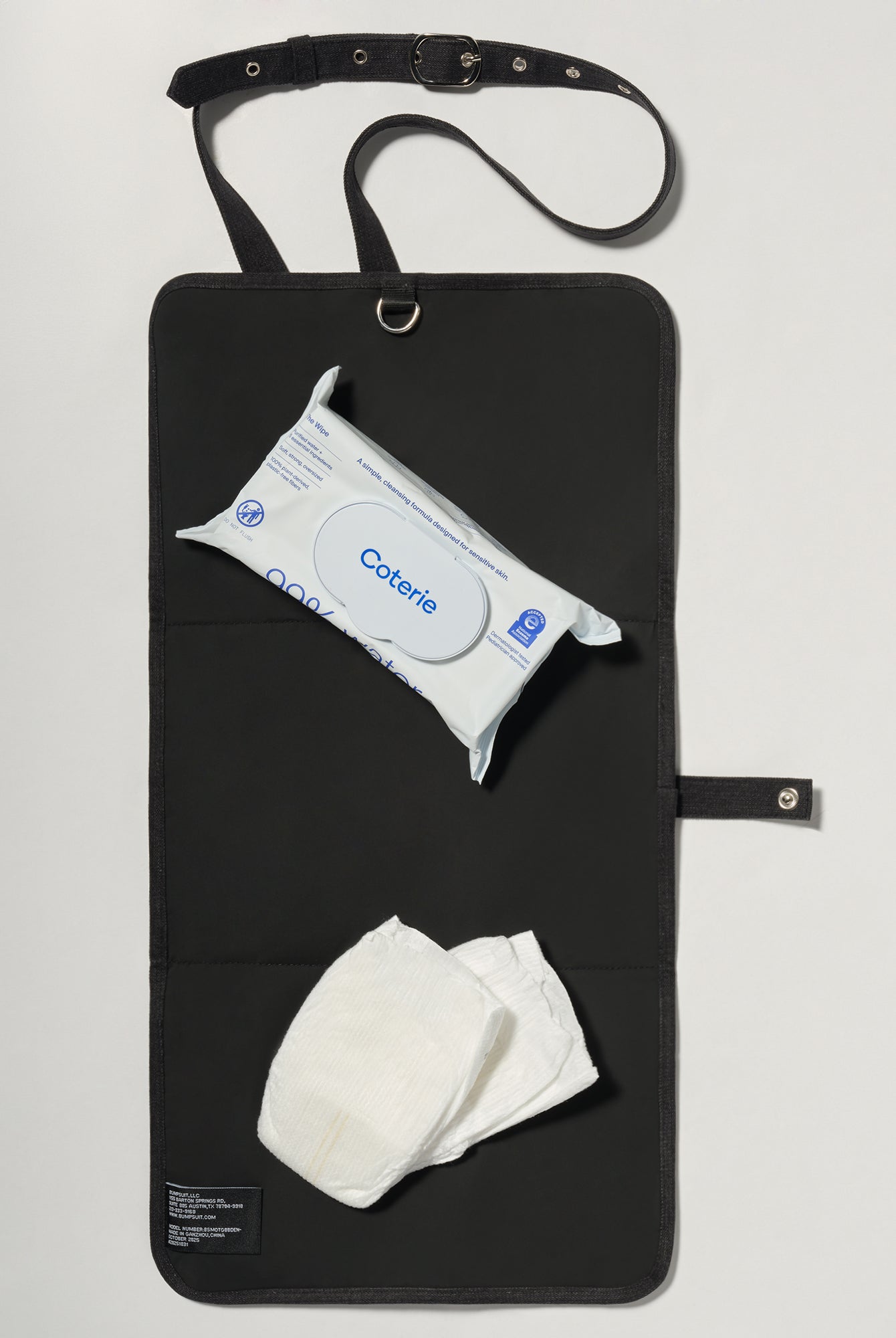 A black denim roll up diaper change mat bag by Spell and Bumpsuit,, shown on a light gray background with wipes and diapers