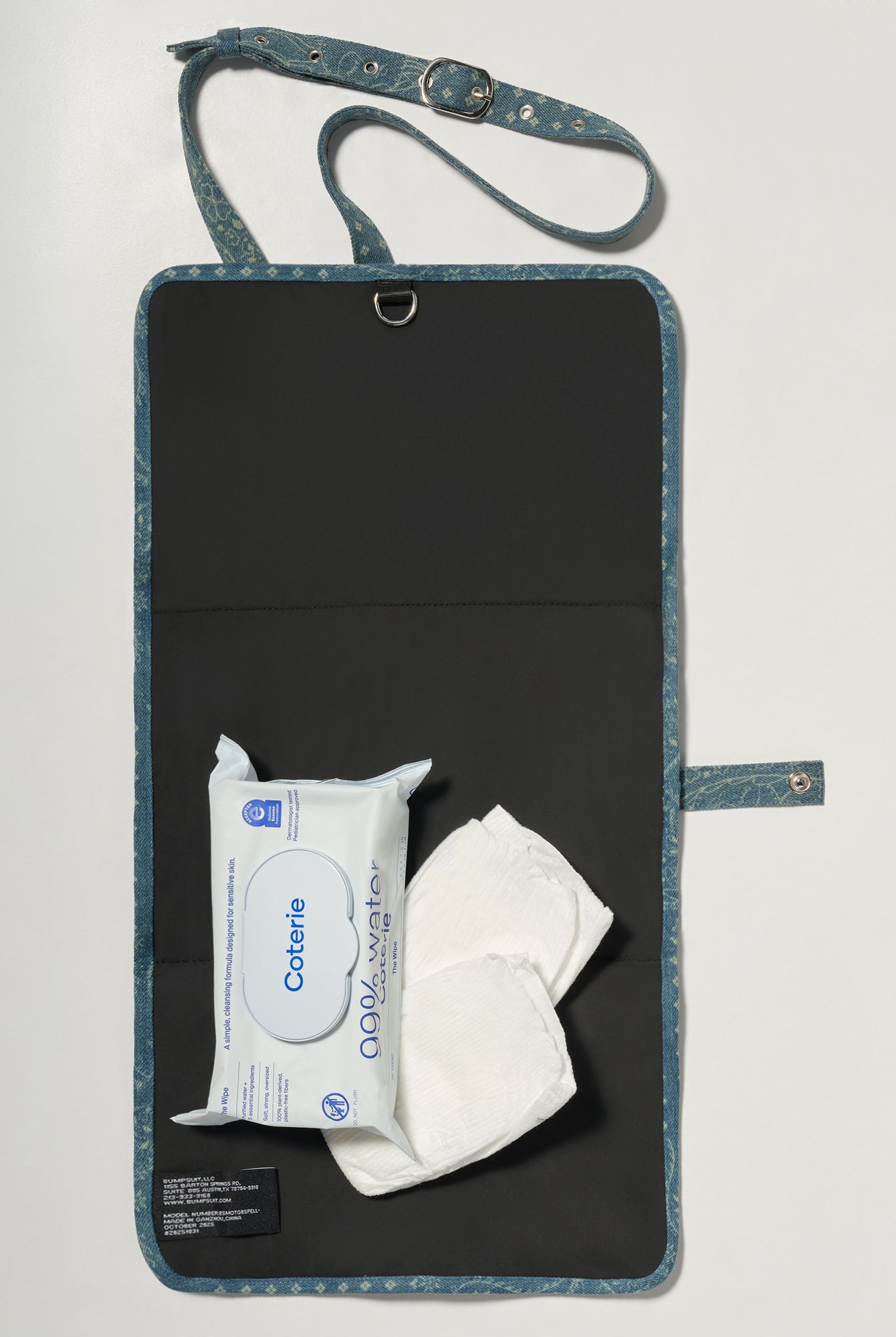 A black denim roll up diaper change mat bag by Spell and Bumpsuit,, shown on a light gray background with wipes and diapers