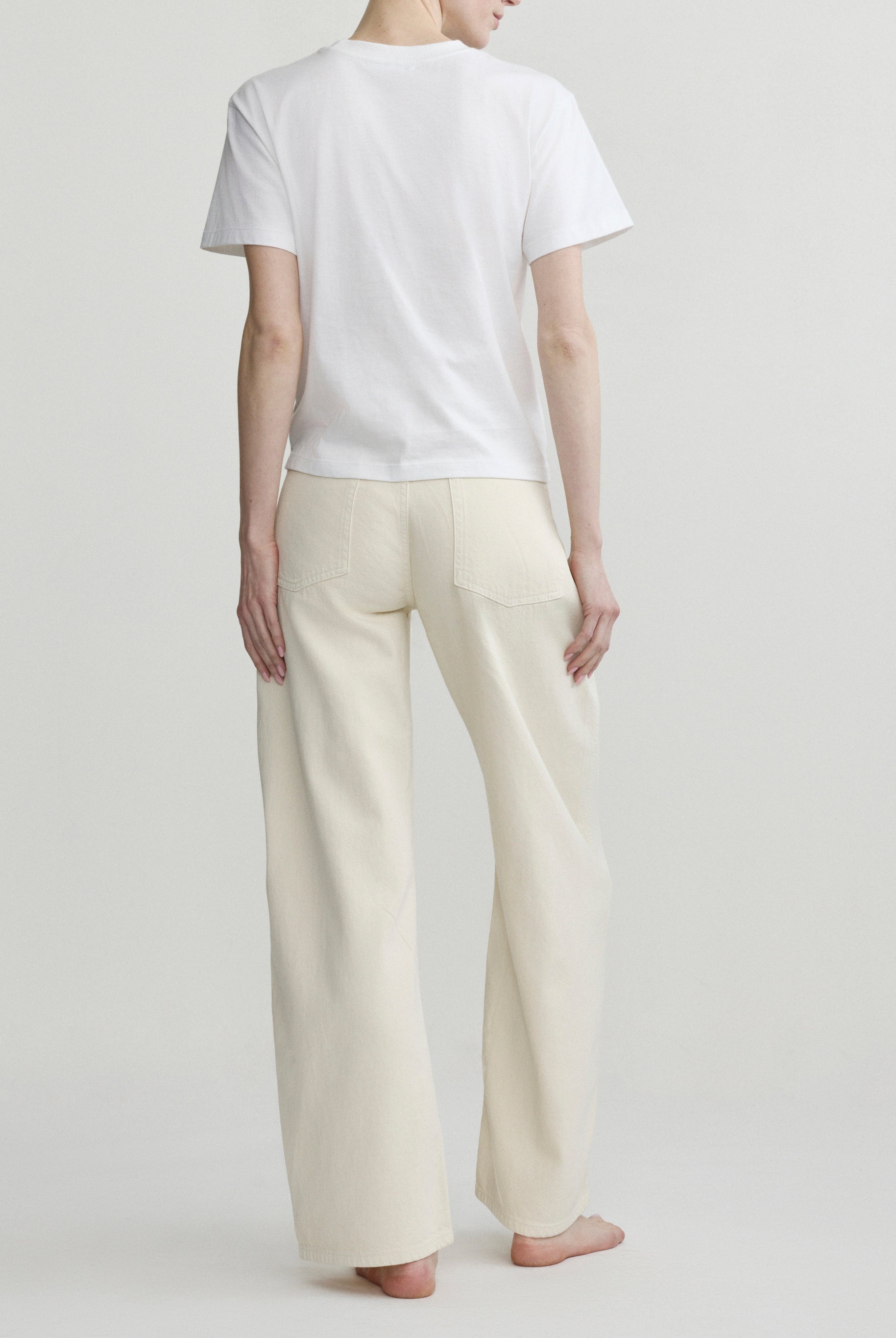 Back view of a person wearing a white t-shirt and beige pants on a plain background