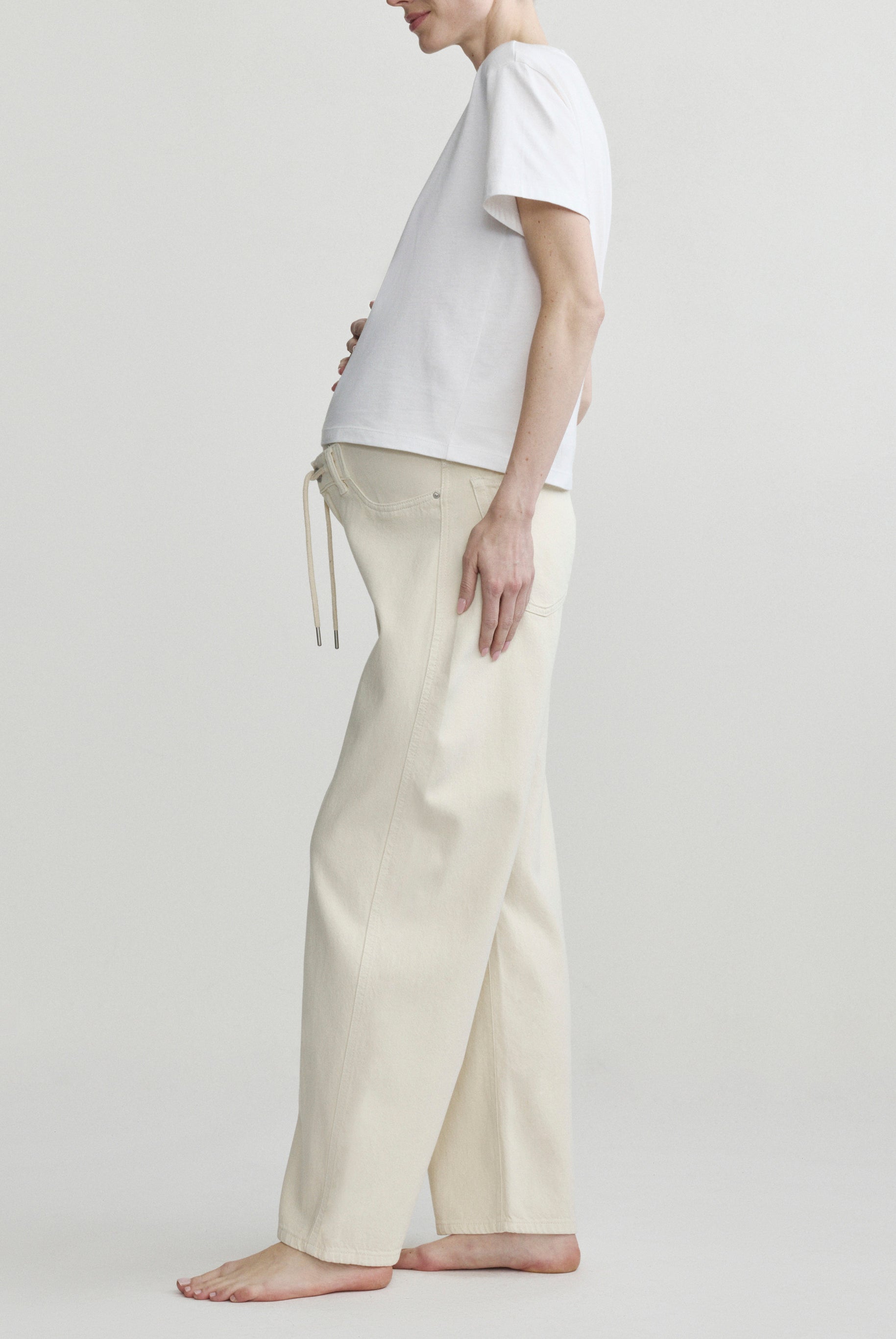 Pregnant person wearing a white t-shirt and beige pants on a plain background