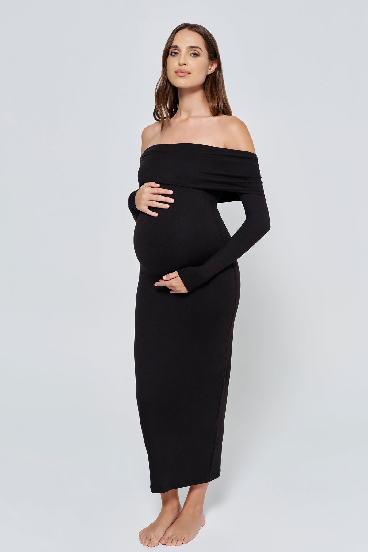 Pregnant woman wearing a black off-shoulder dress against a white background