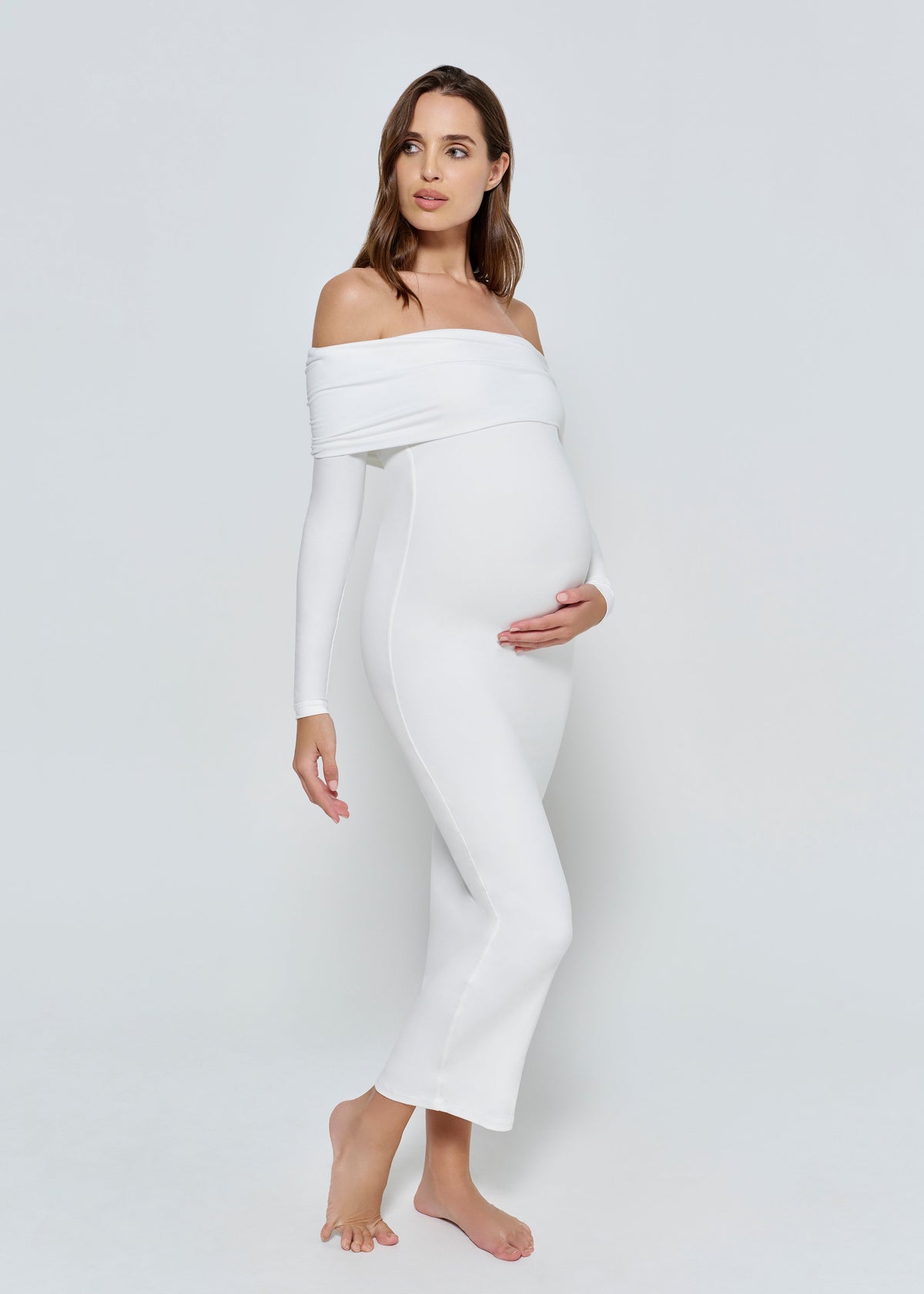 Pregnant woman wearing a ivory Bumpsuit off-shoulder dress on a white background