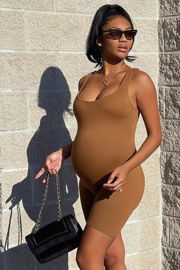 pregnant woman wearing the Cindy Scoop neck romper by Bumpsuit standing against a brick wall