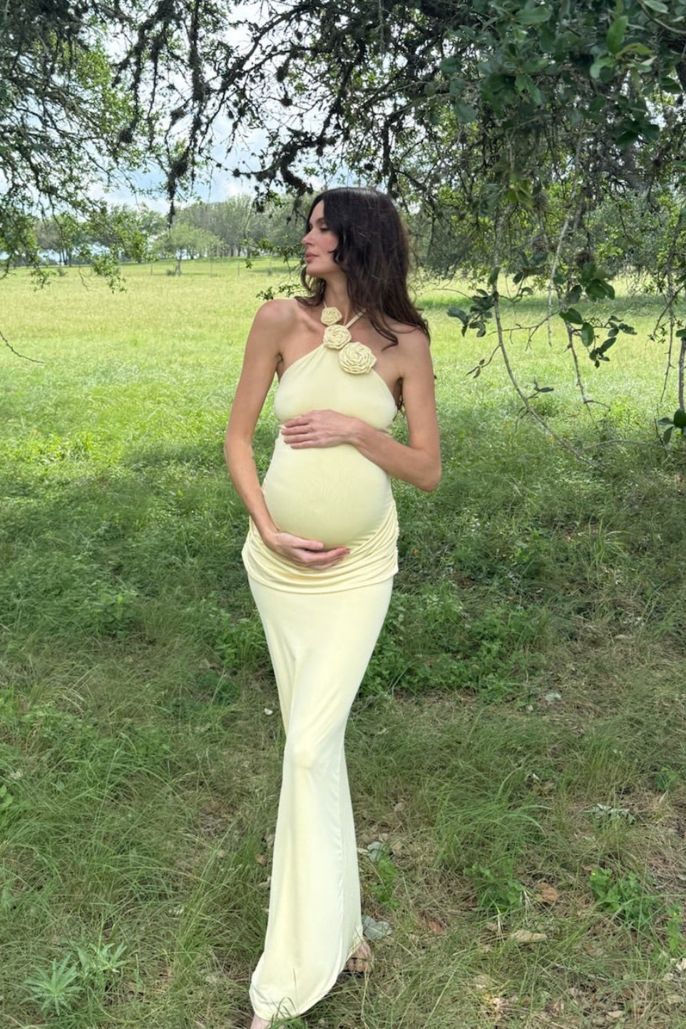 Full-length view of The Jenny Dress on a pregnant model, showcasing its butter yellow floral halter neckline and maxi length
