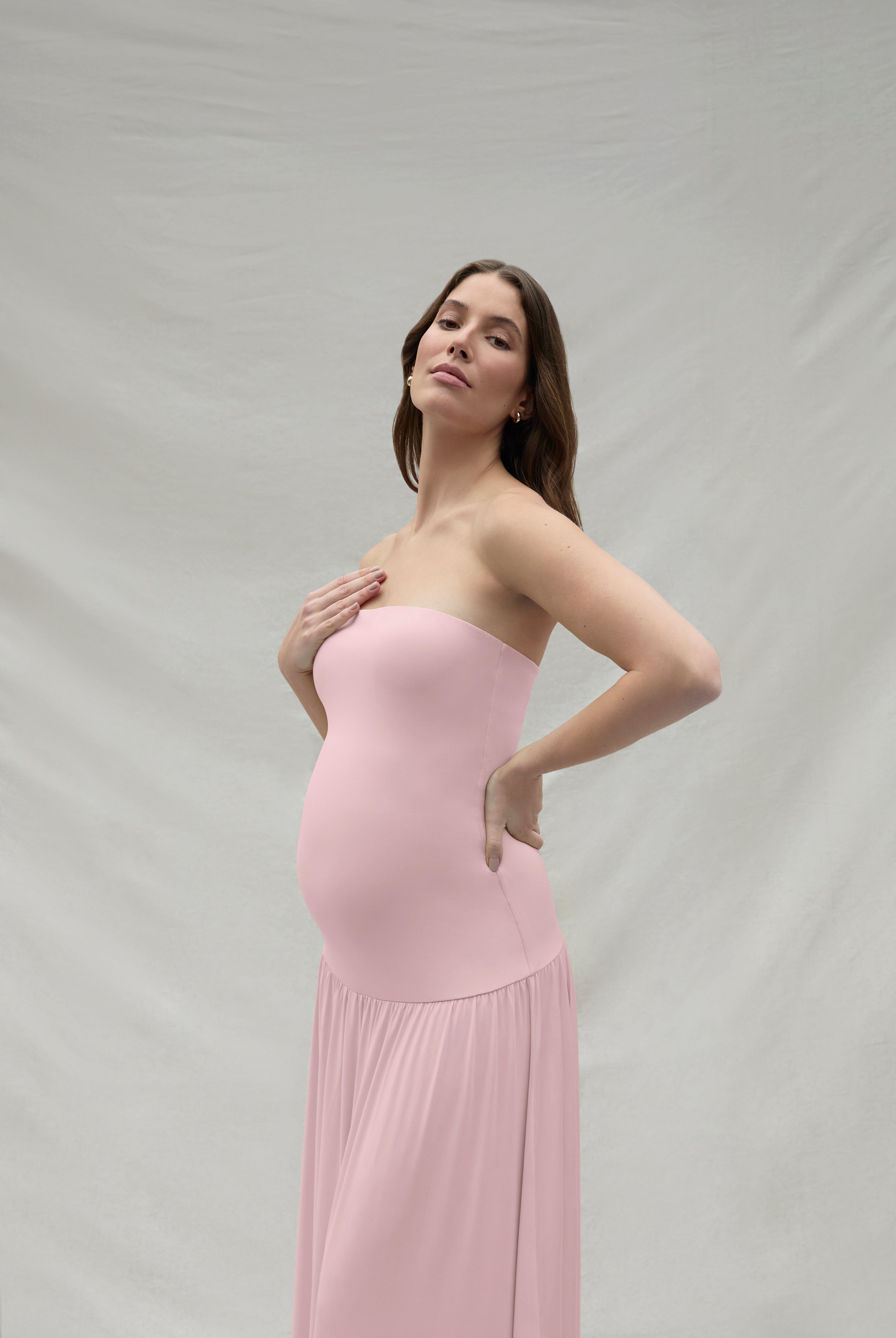 Woman wearing a pink strapless maternity dress against a plain background