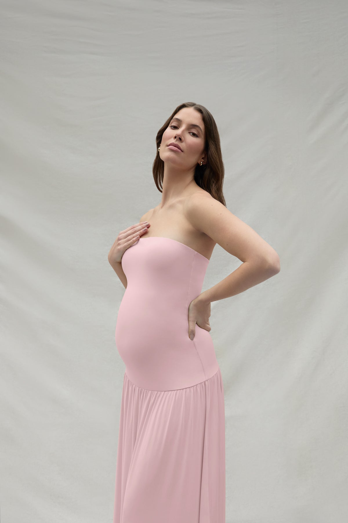Woman wearing a pink strapless maternity dress against a plain background