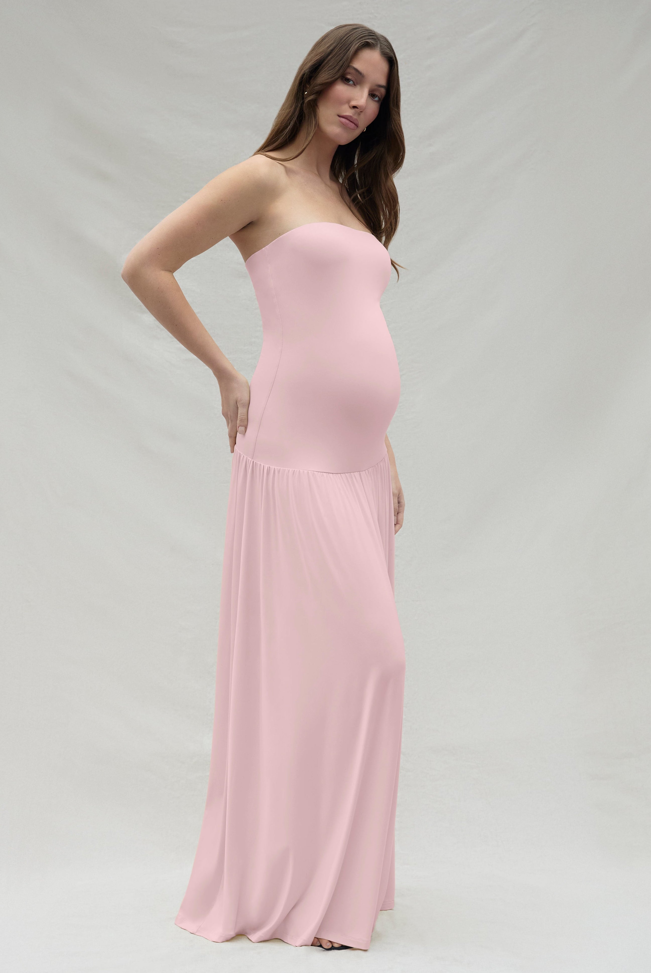 Woman wearing a strapless maternity pink dress against a plain background