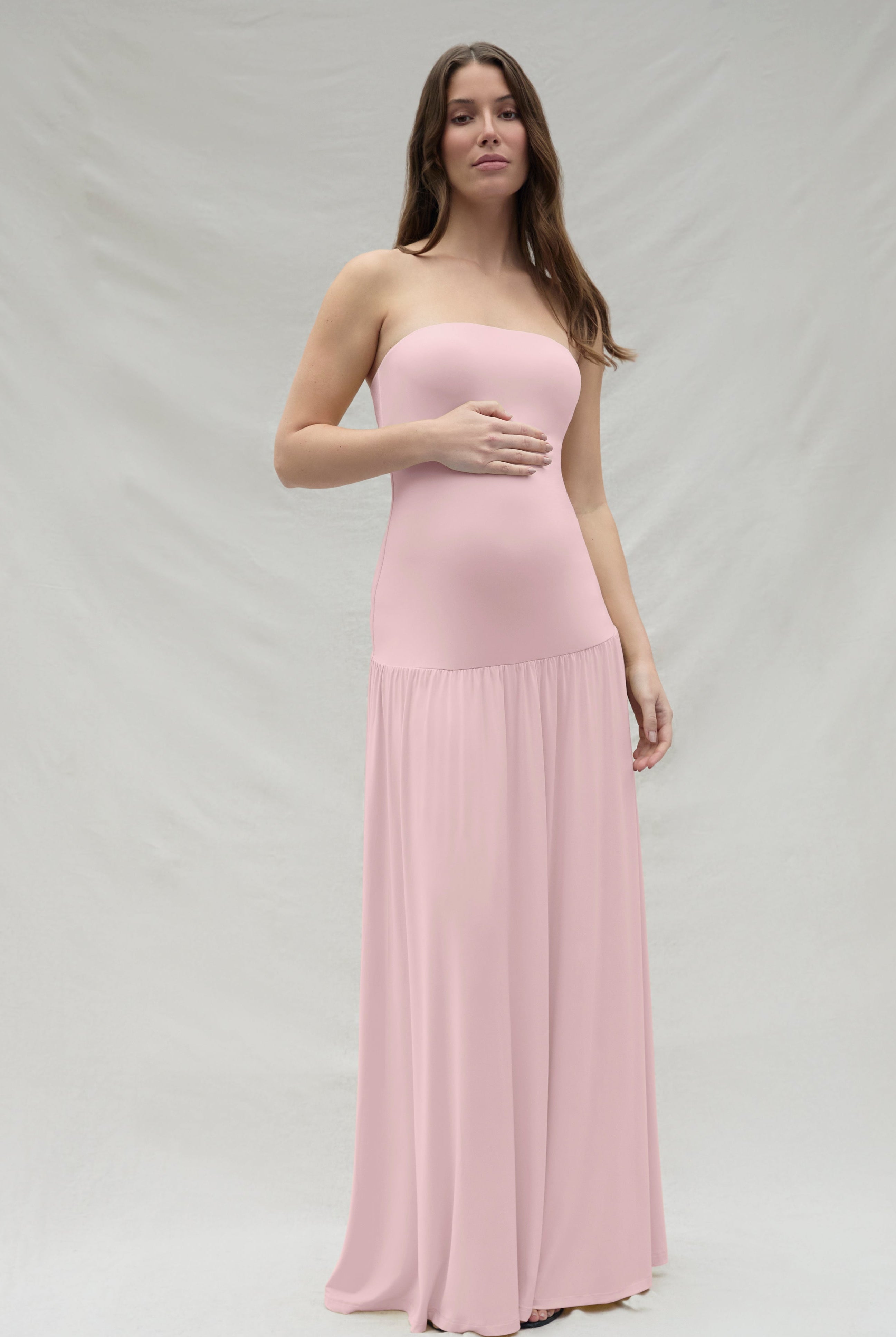 Woman wearing a pink strapless Bumpsuit gown against a white background