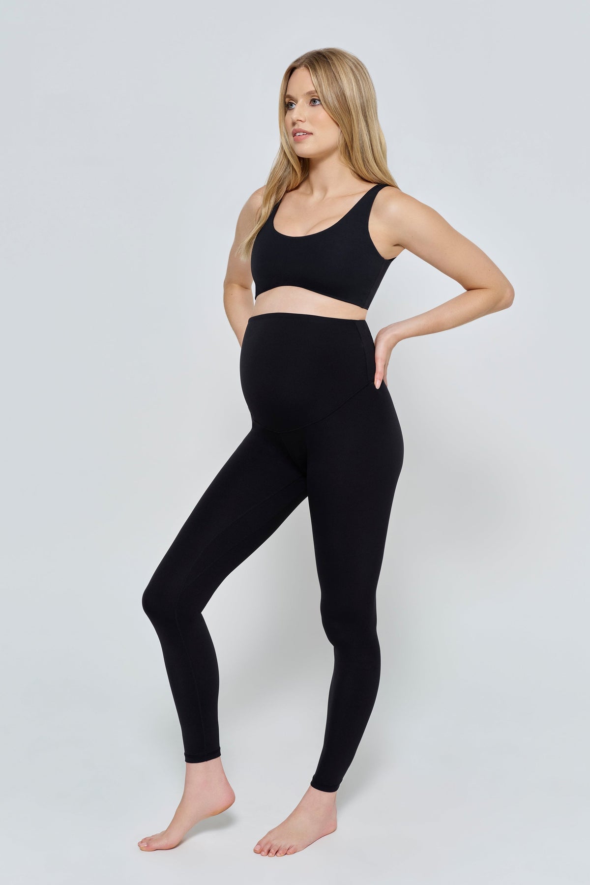 Front three quarter view of The Perfect Movement Maternity Legging in black with an over bump waistband on a model against a light gray background