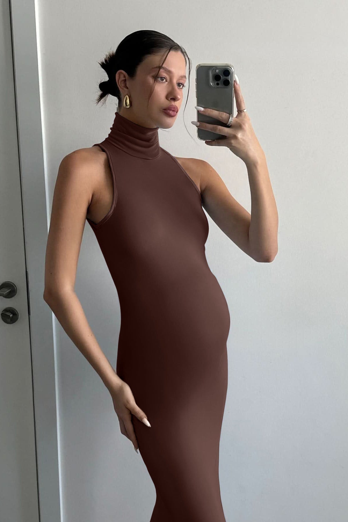 A pregnant woman wearing the serena turtleneck sleeveless maternity maxi dress in chocolate brown