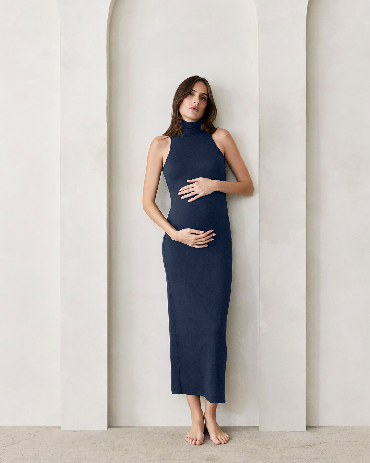 Pregnant women holding her belly wearing Bumsuits Serena turtleneck sleeveless dress in Navy