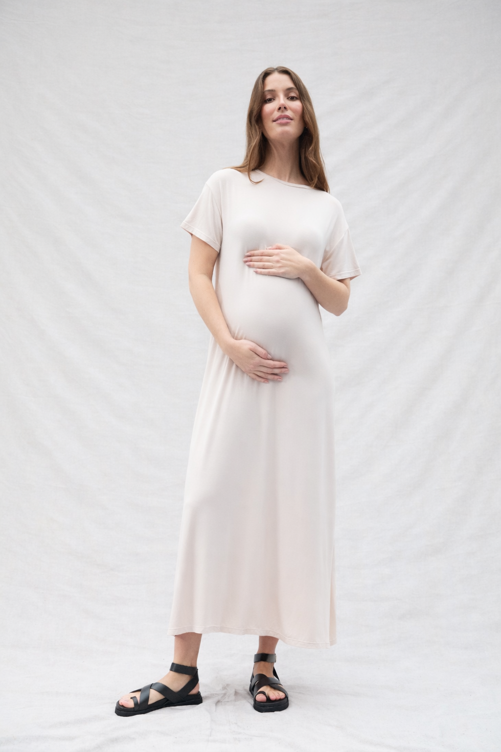 Pregnant woman wearing an oat-colored dress against a white background