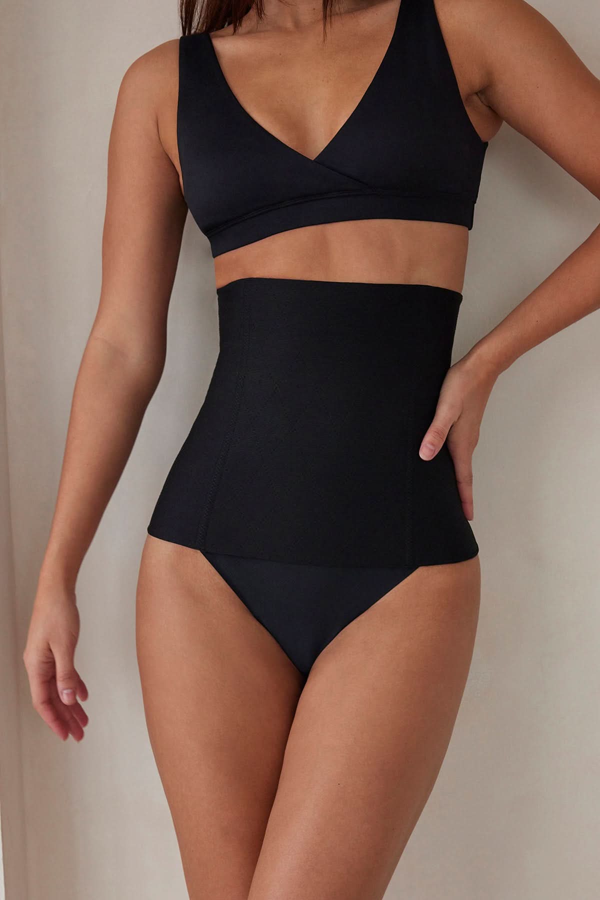 Woman wearing the postpartum support waist trainer in black by bumpsuit