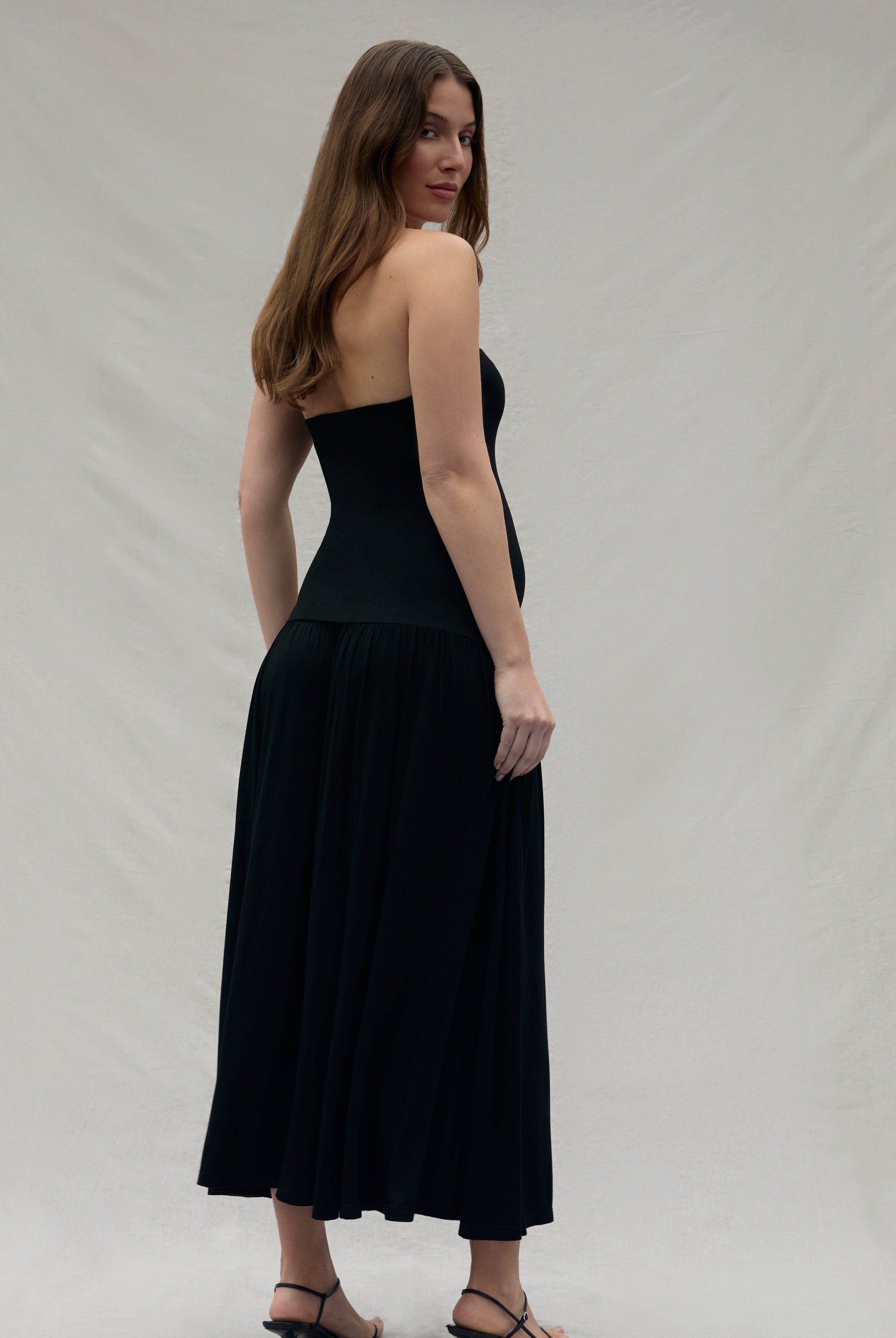 Woman wearing a black strapless dress against a plain background