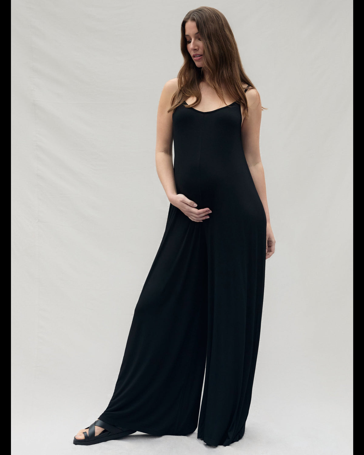 Pregnant woman wearing a black sleeveless cotton jumpsuit on a white background
