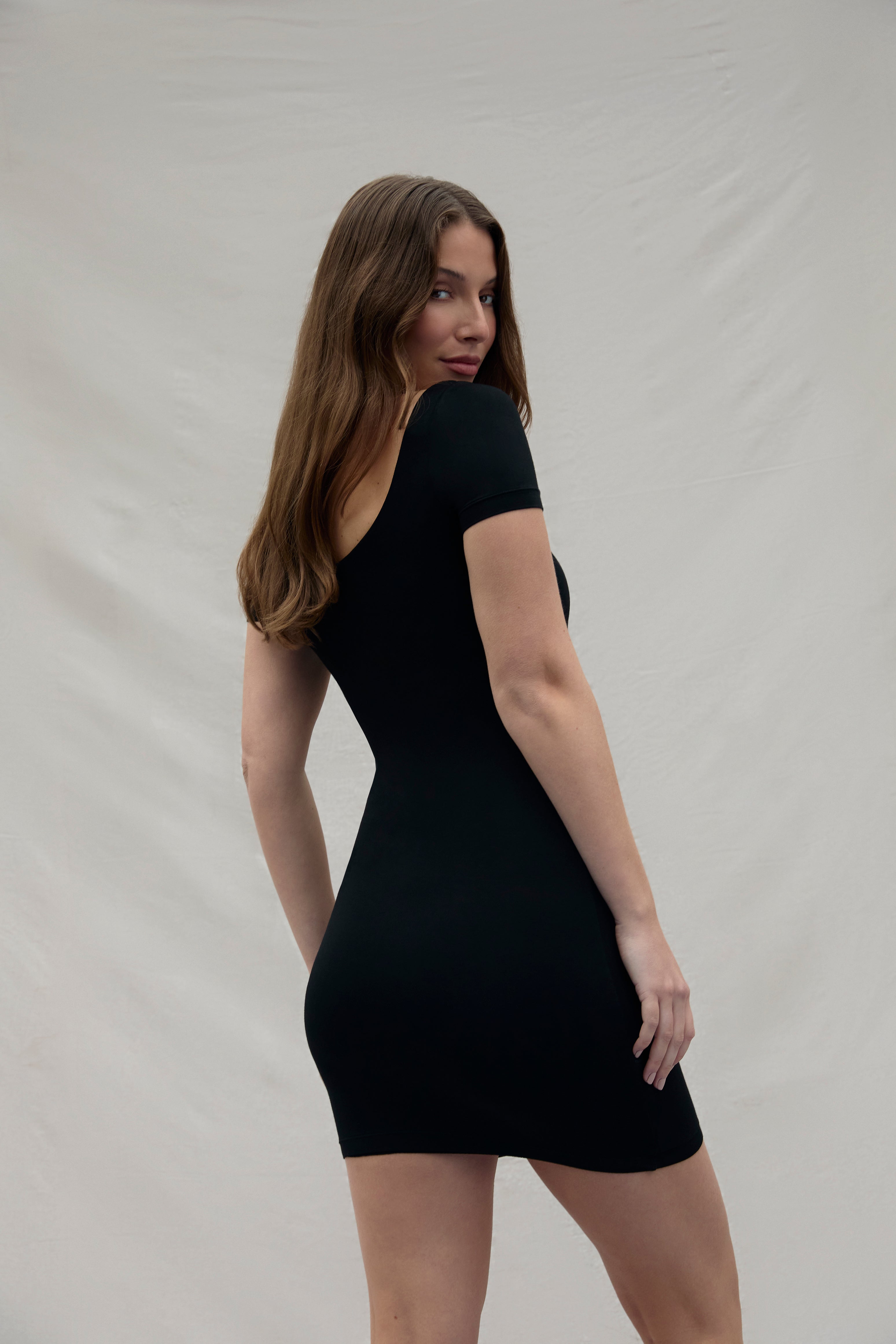 back view of a woman wearing a black dress against a plain background