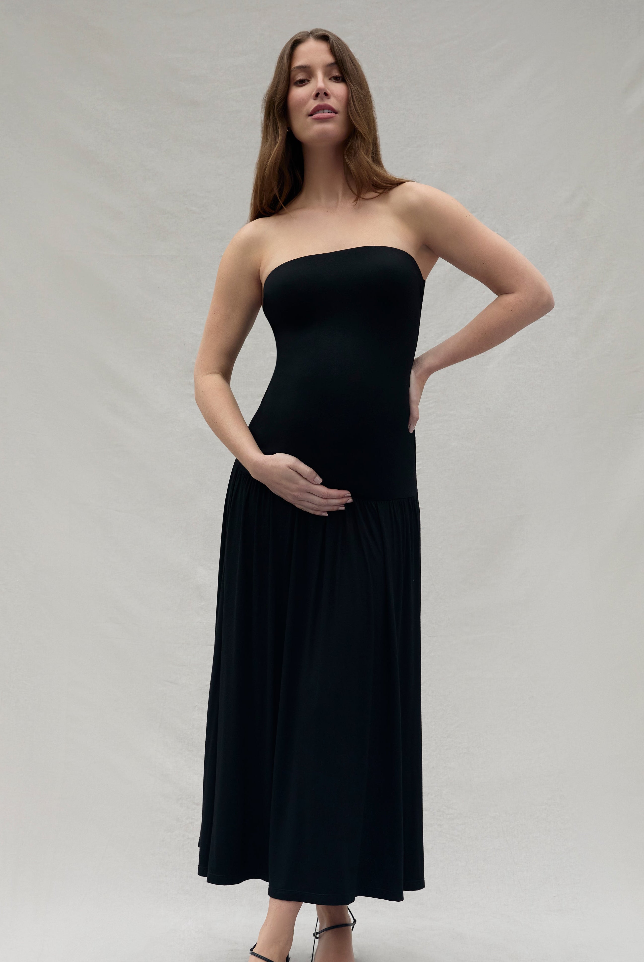 Woman wearing a Bumpsuit black strapless dress against a plain background