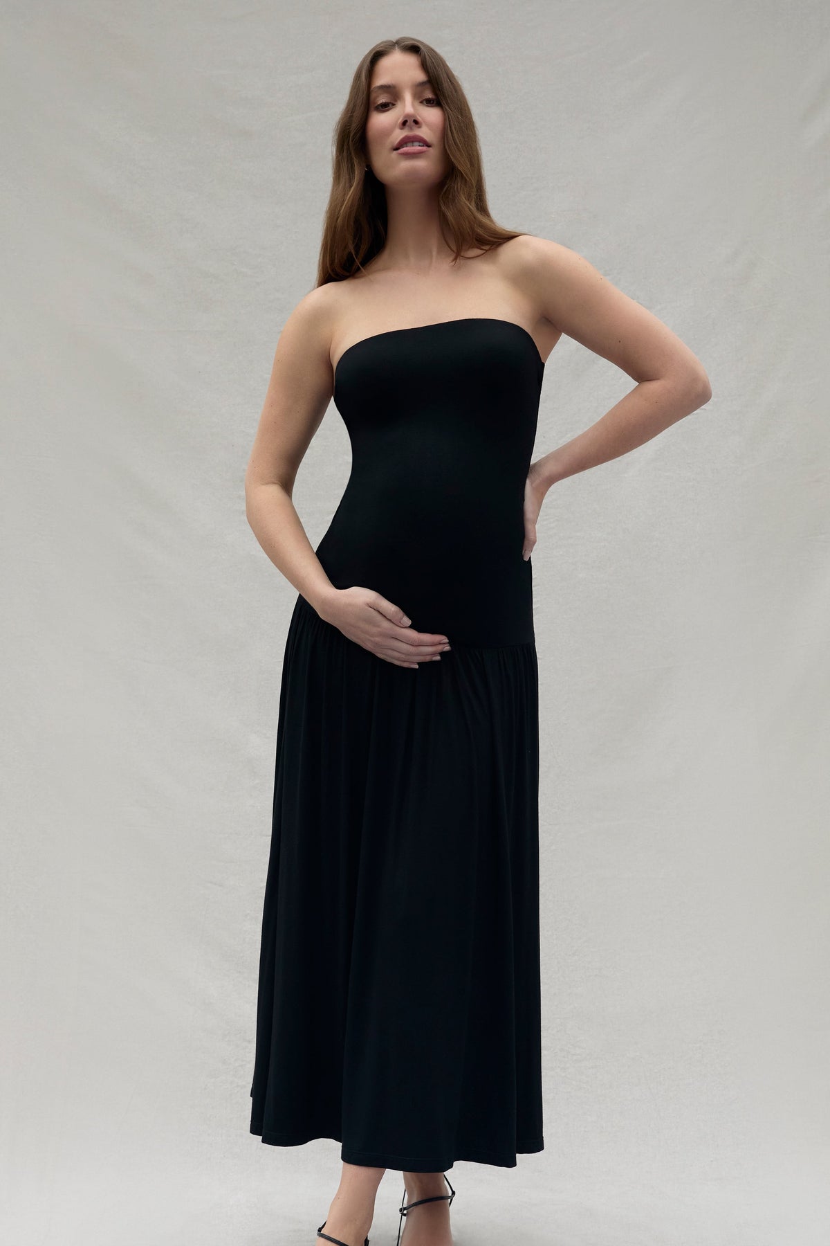 Woman wearing a Bumpsuit black strapless dress against a plain background