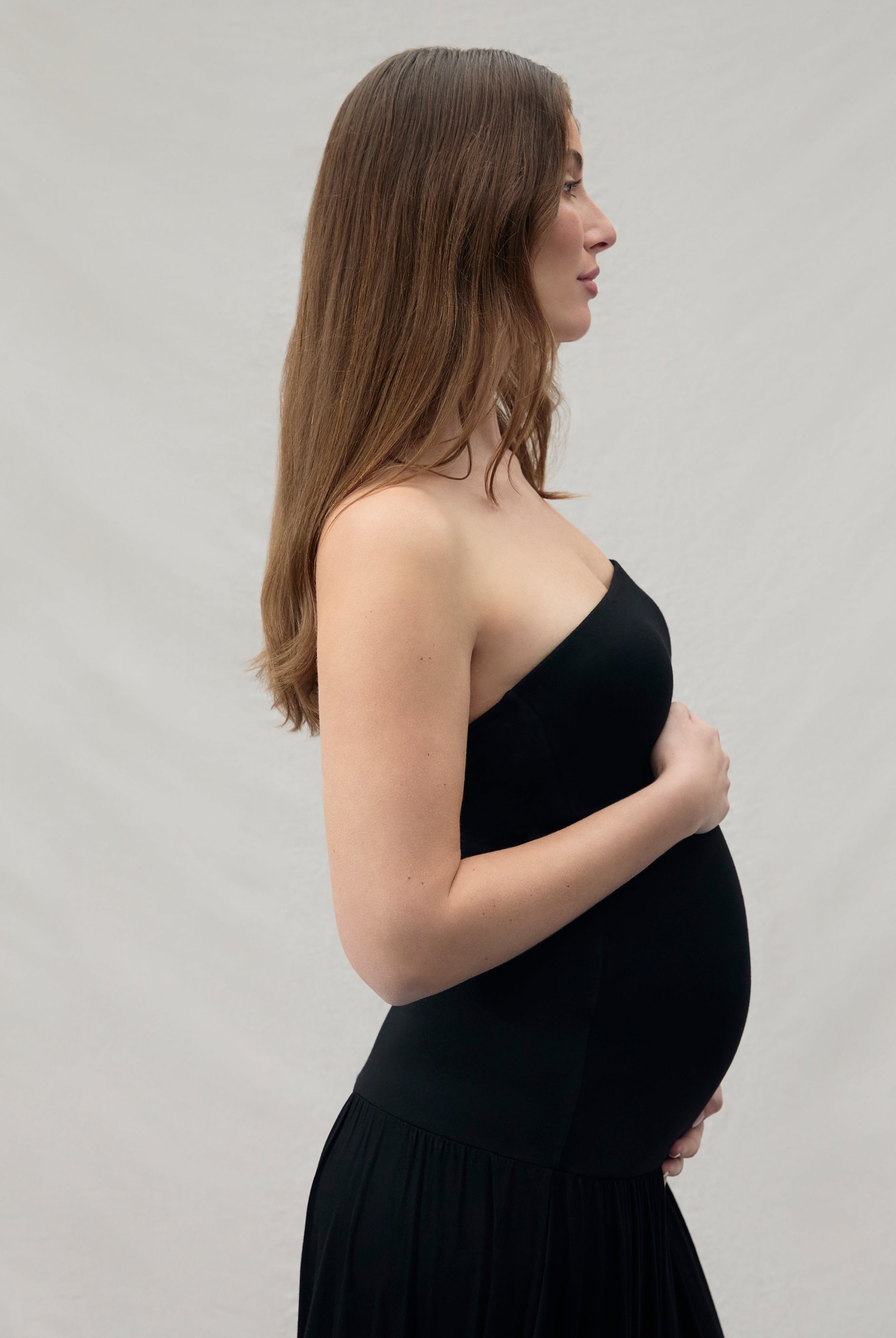 Pregnant woman wearing a black dress against a plain background