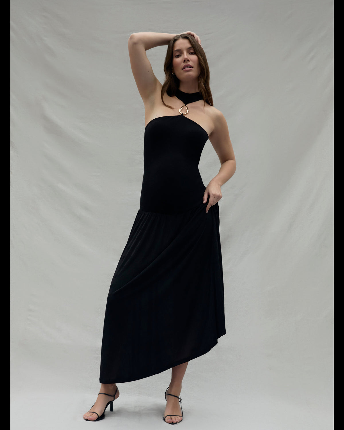 Pregnant woman wearing a black strapless halter dress with a gold halter accent against a plain background