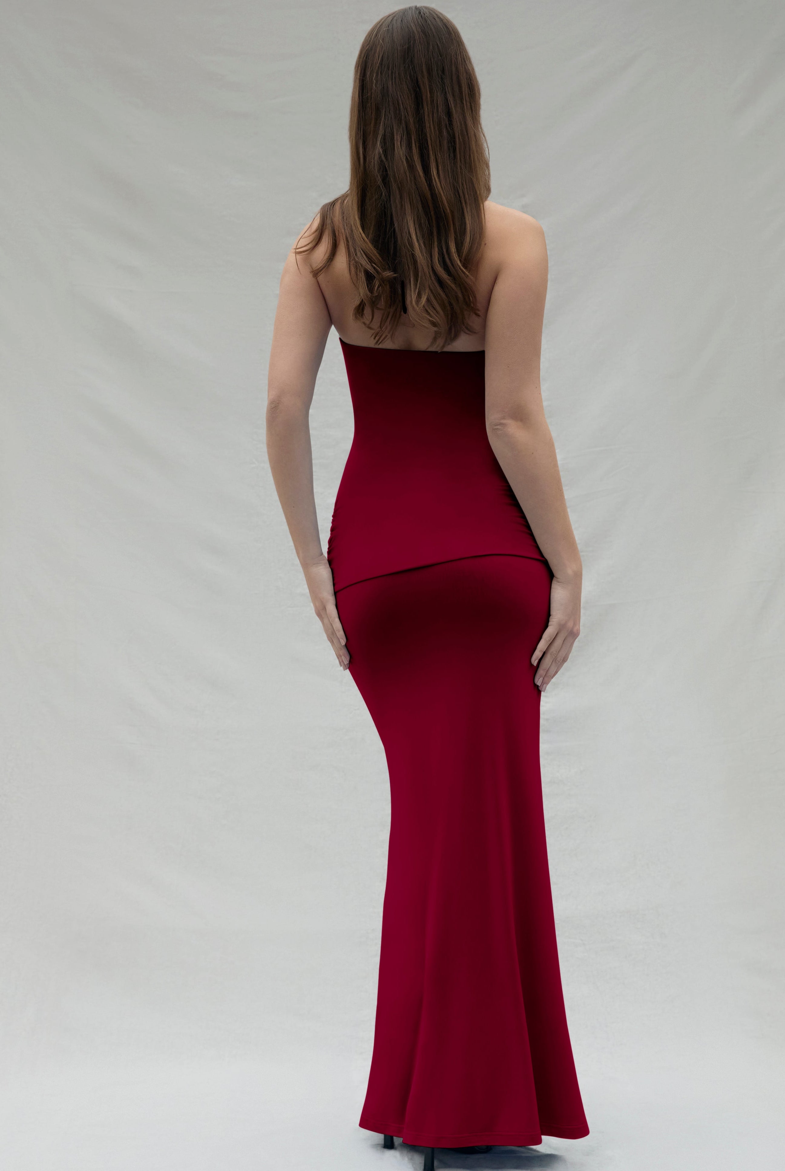 backview of a woman wearing a burgundy maxi Bumpsuit dress on a white background
