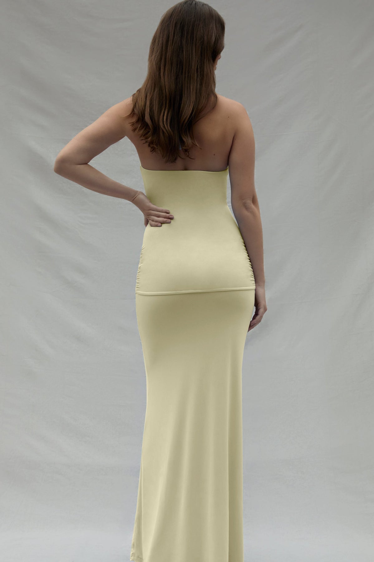 Back view of a woman wearing a yellow dress against a plain background