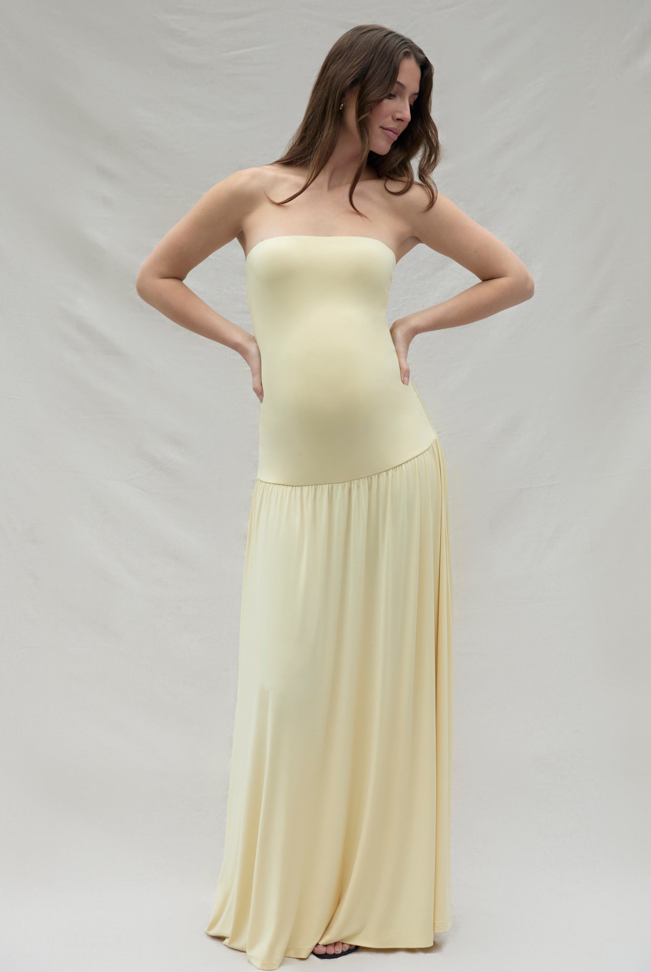 Pregnant woman wearing a maternity Bumpsuit strapless yellow dress against a plain background