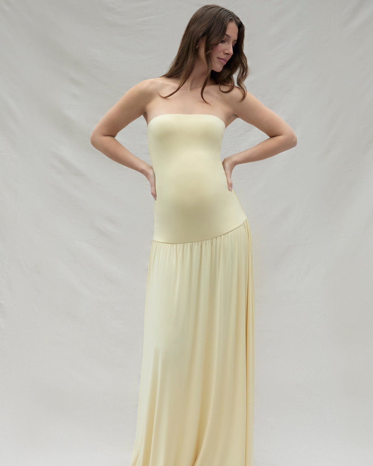 Pregnant woman wearing a maternity Bumpsuit strapless yellow dress against a plain background