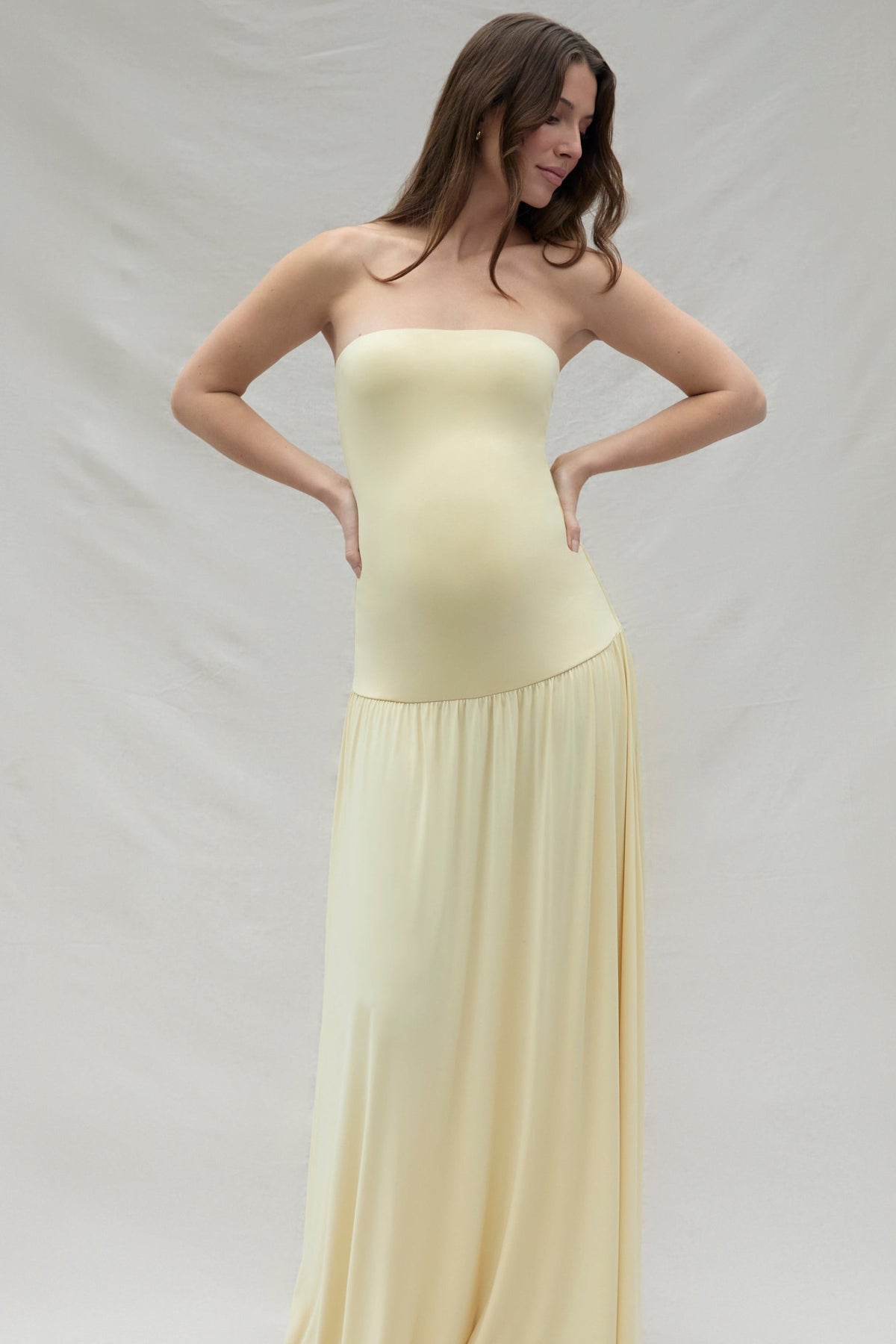Pregnant woman wearing a maternity Bumpsuit strapless yellow dress against a plain background