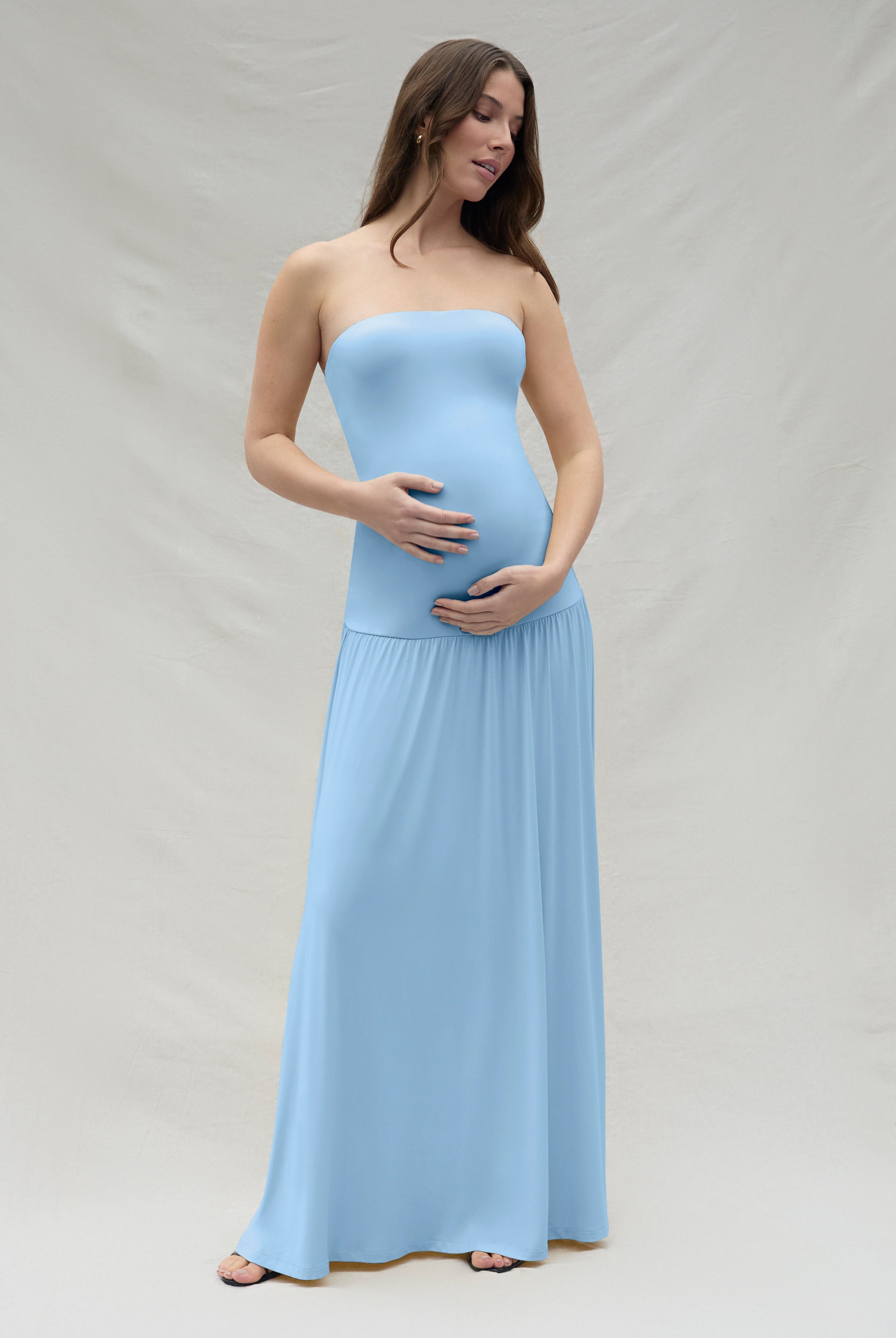 Pregnant woman wearing a powder blue strapless maternity gown against a plain background
