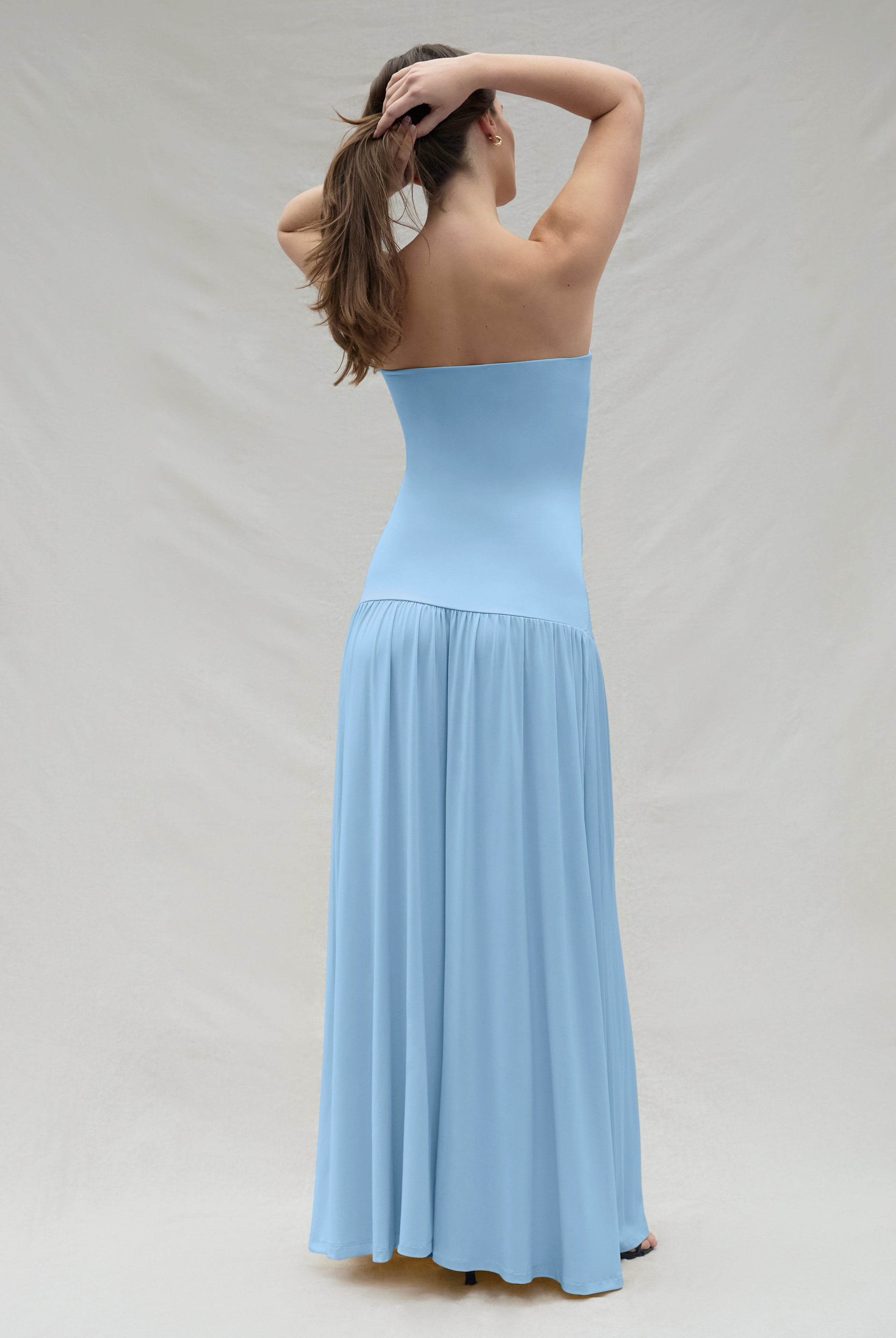 Back view of a woman wearing a powder blue strapless gown against a plain background