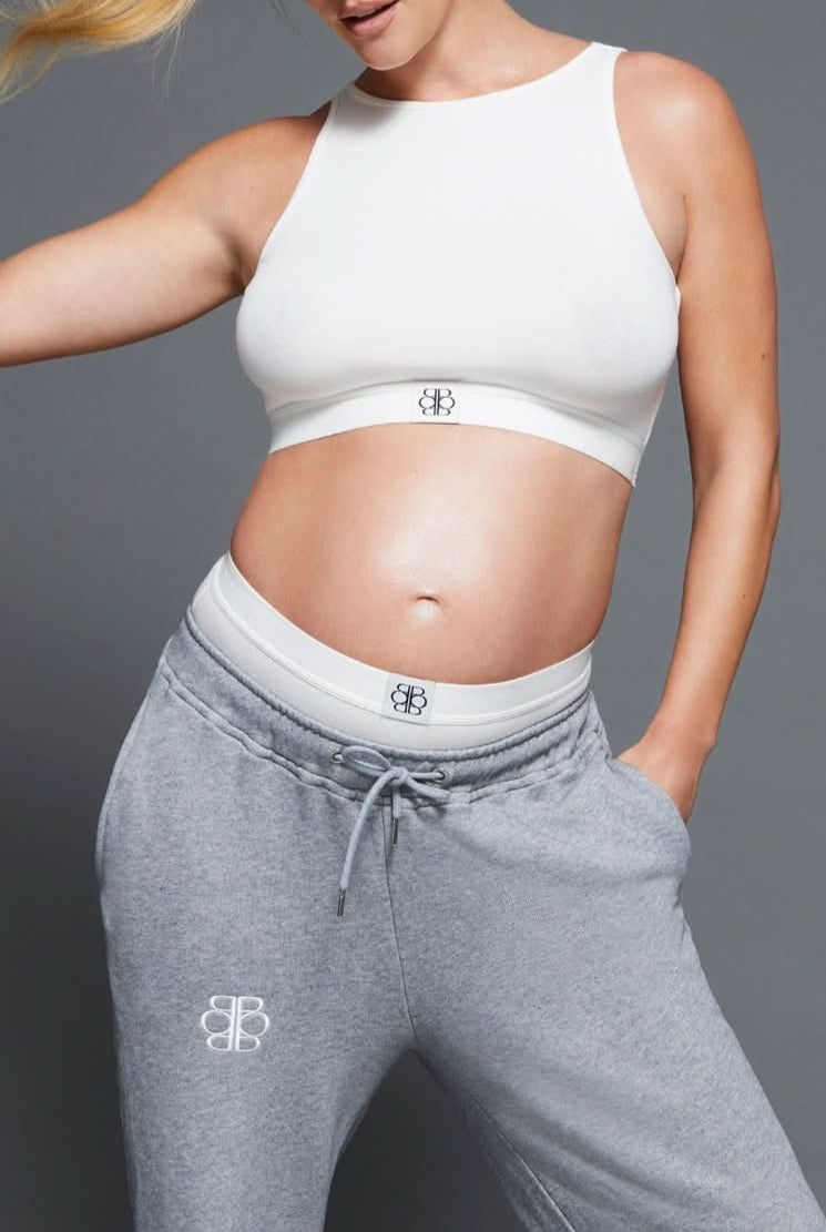 Person wearing a white sports bra and gray sweatpants with a Bumpsuit logo on a gray background