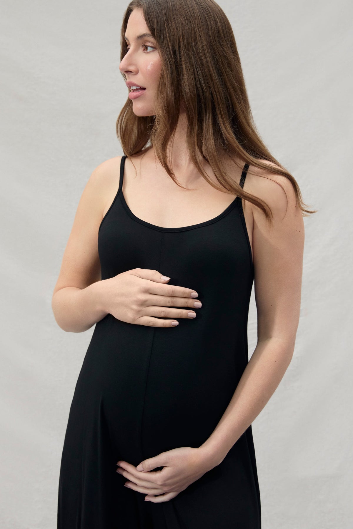 pregnant woman wearing a Bumpsuit black jumpsuit holding her belly and looking away