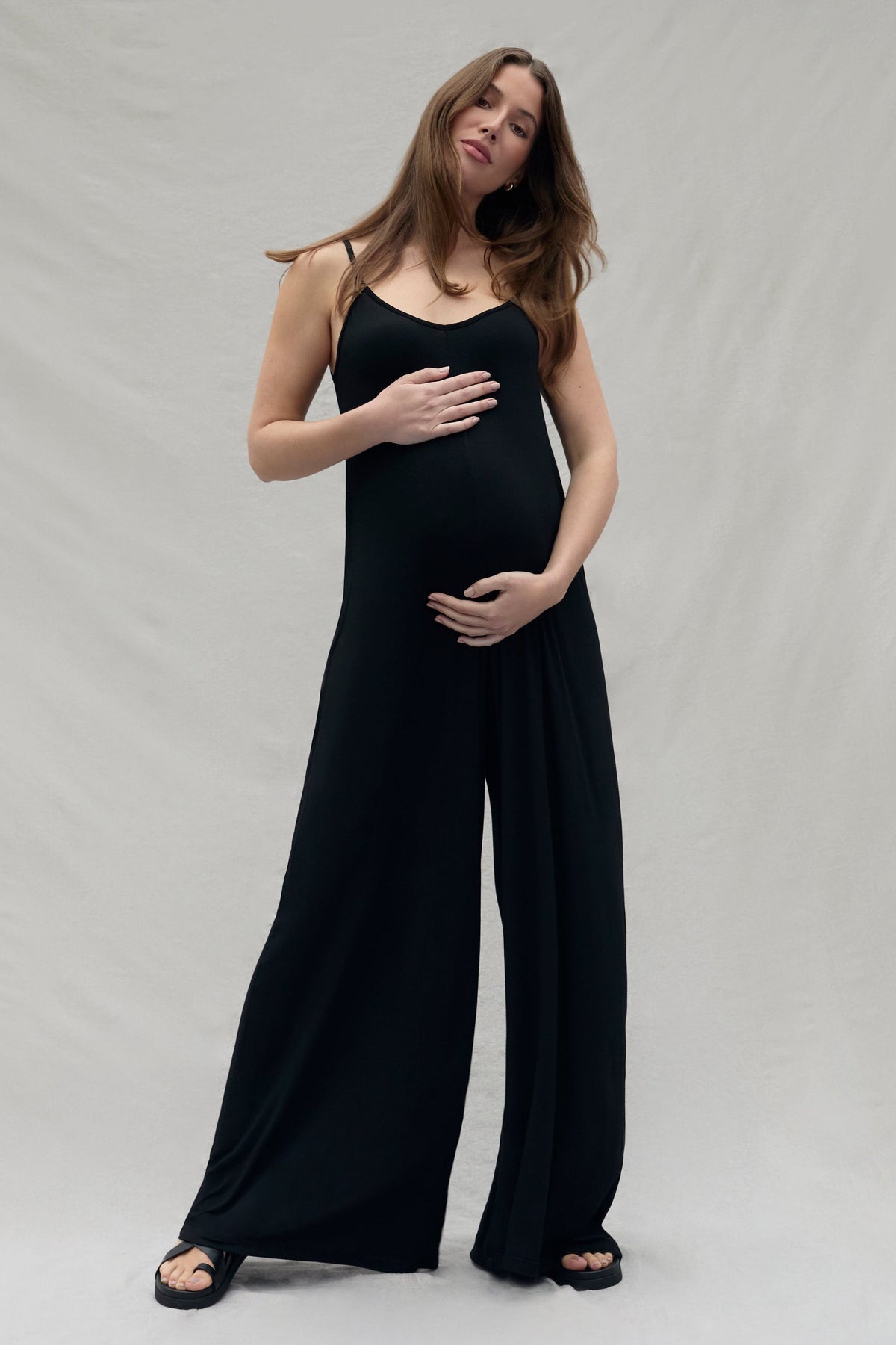 pregnant woman wearing a black cotton jumpsuit against a plain background