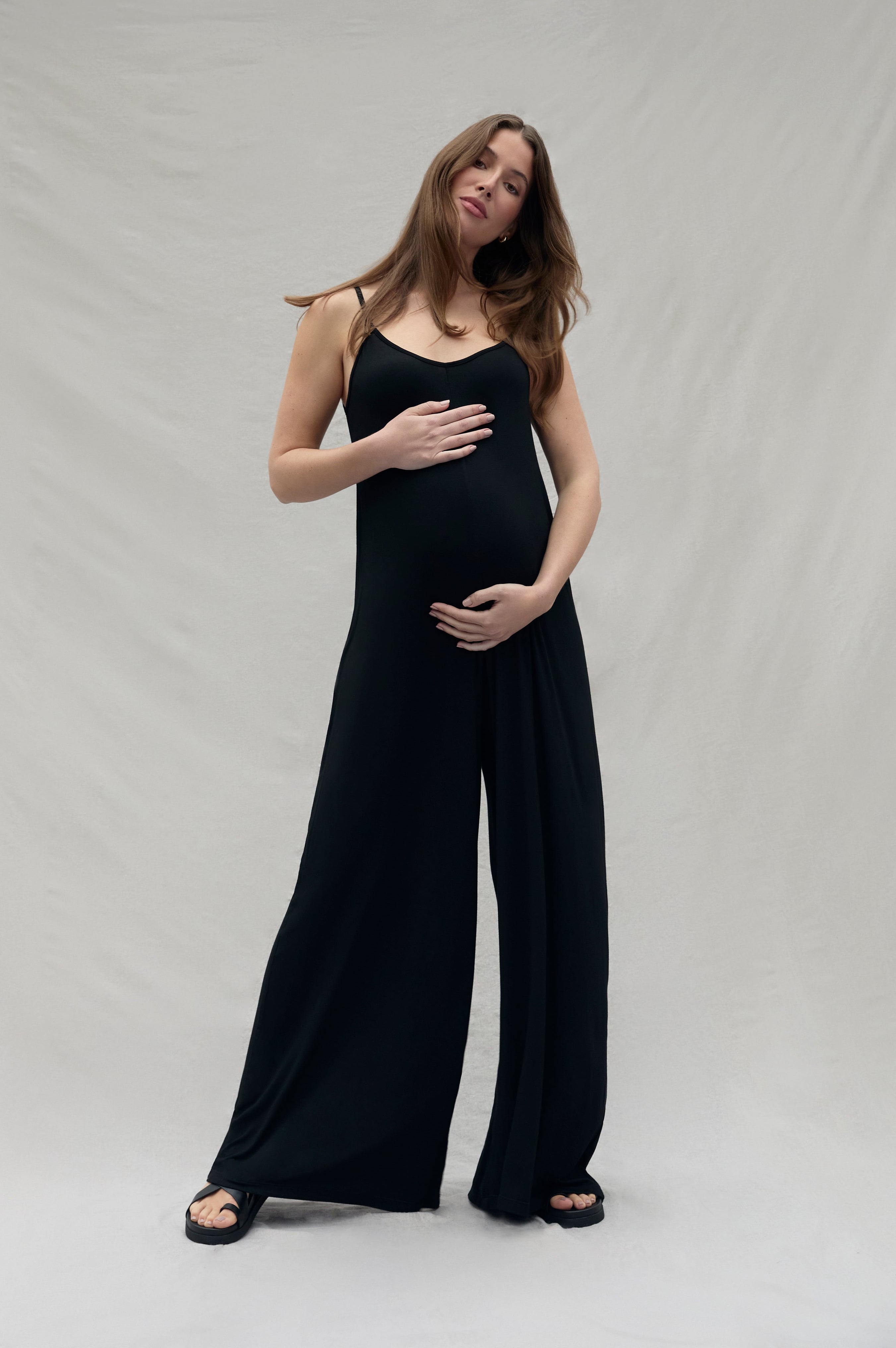 pregnant woman wearing a black cotton jumpsuit against a plain background